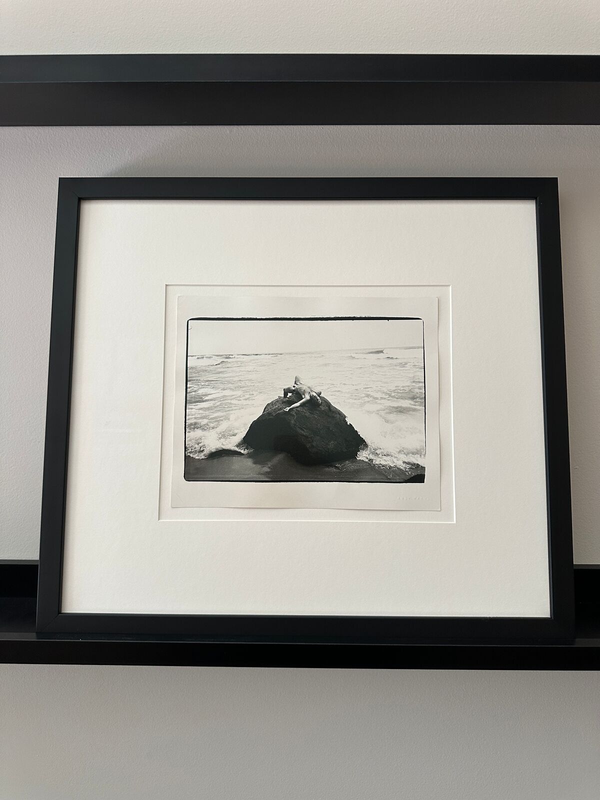 A black and white photo of a person laying on a rock in the ocean.