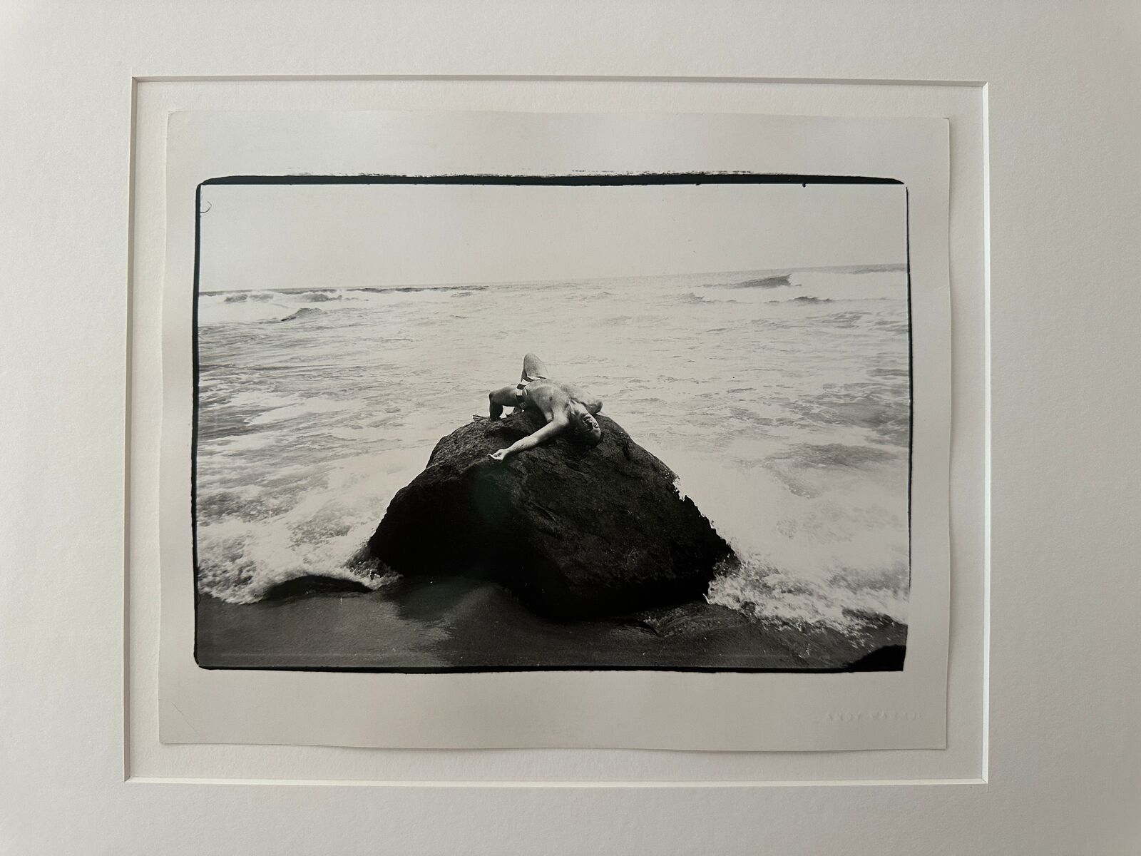 A black and white photo of a person laying on a rock in the ocean.