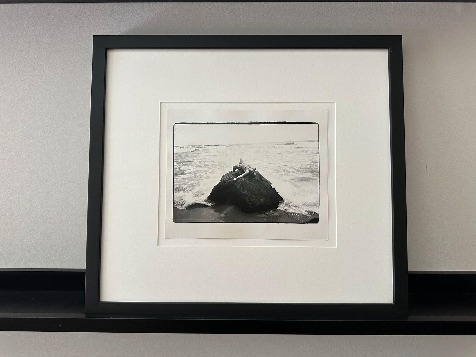 A black and white photo of a person laying on a rock in the ocean.