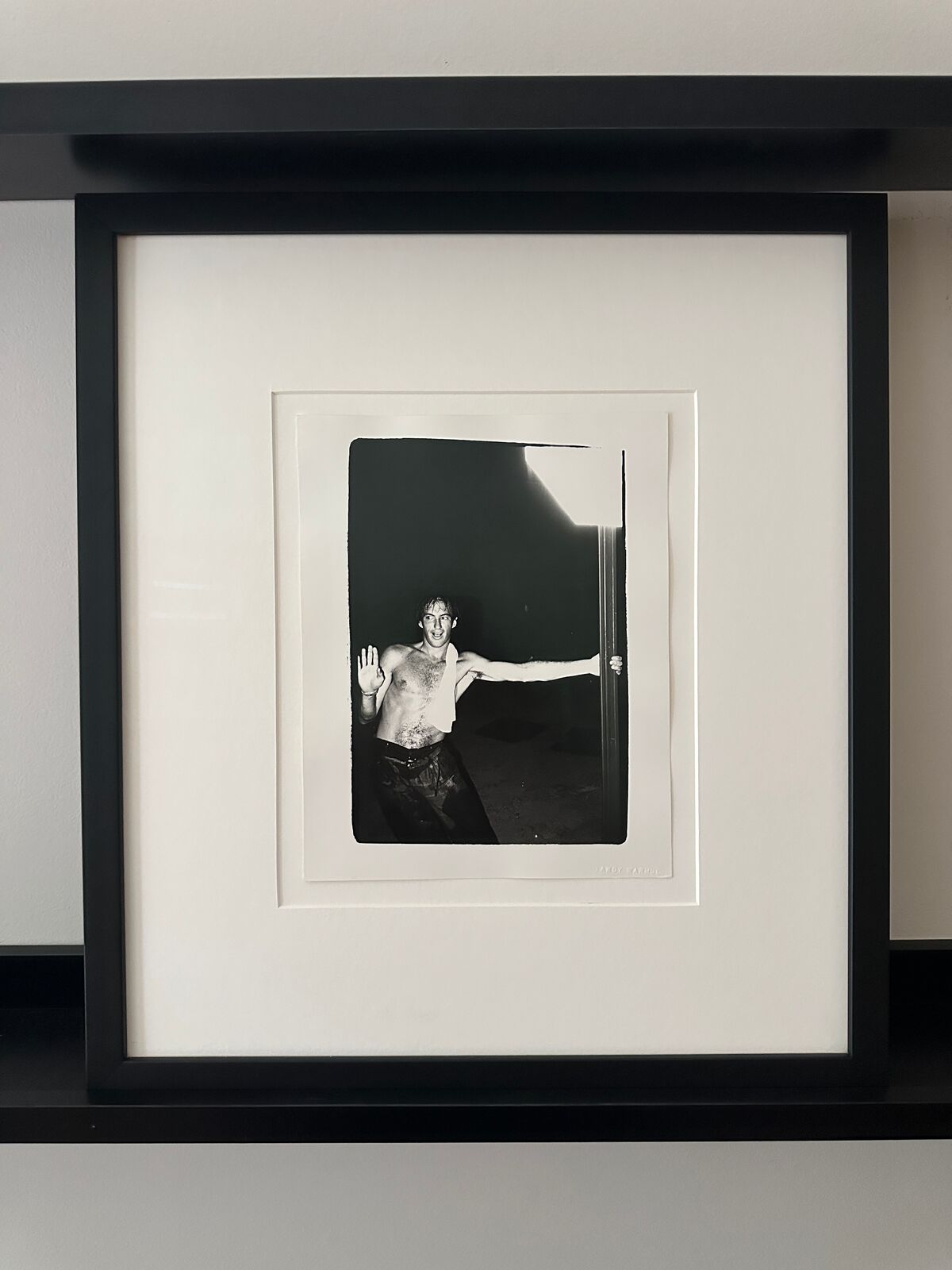 A shirtless man standing in front of a door with his arms outstretched.