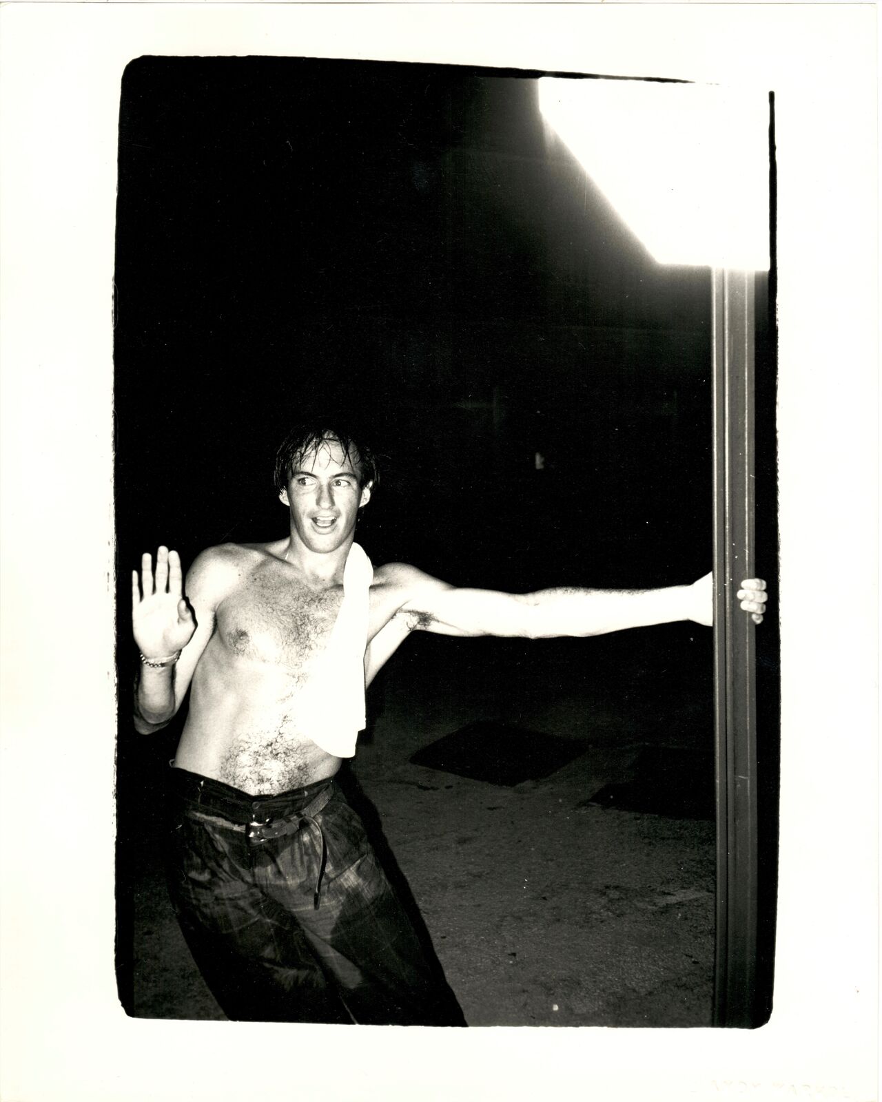 A shirtless man standing in front of a door with his arms outstretched.