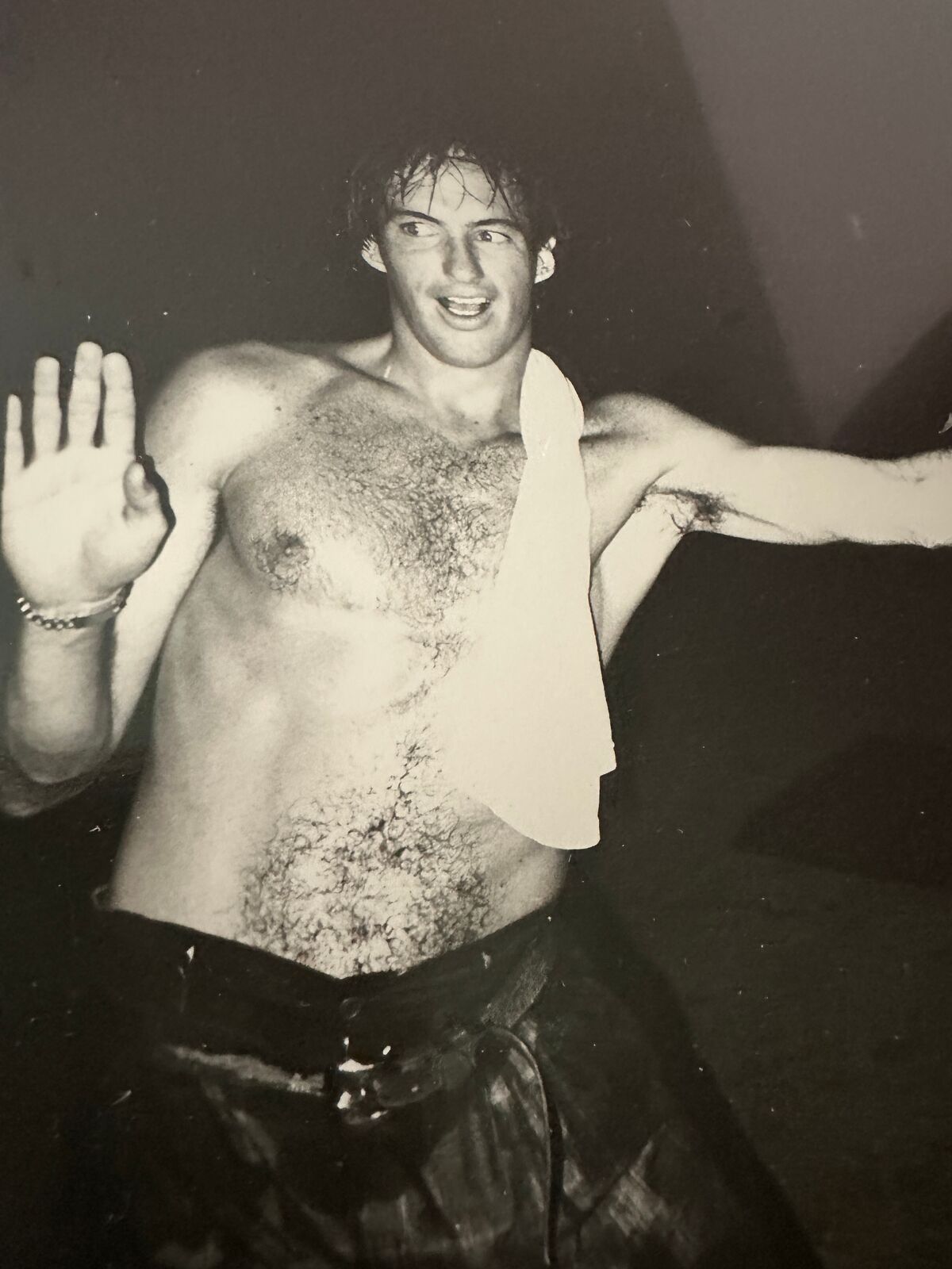 A shirtless man standing in front of a door with his arms outstretched.