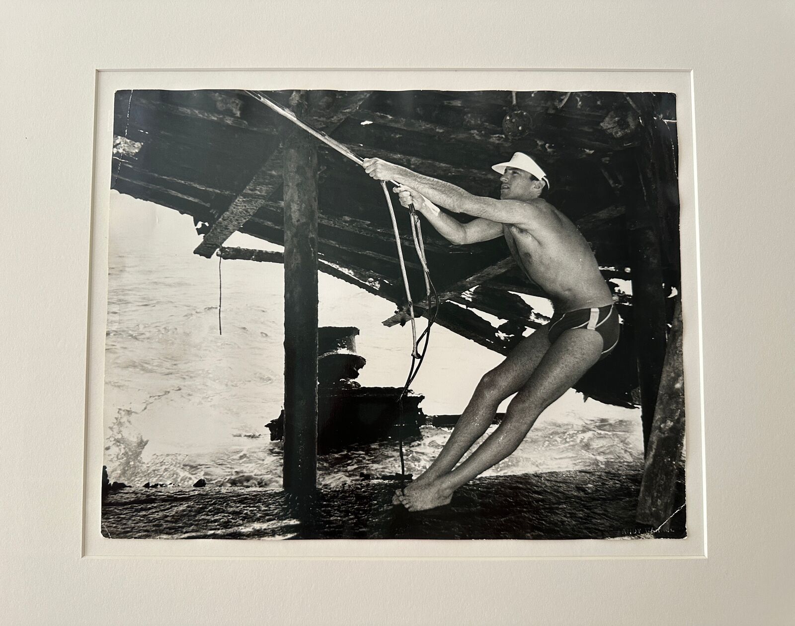 A man in a bathing suit and hat holding onto a rope.