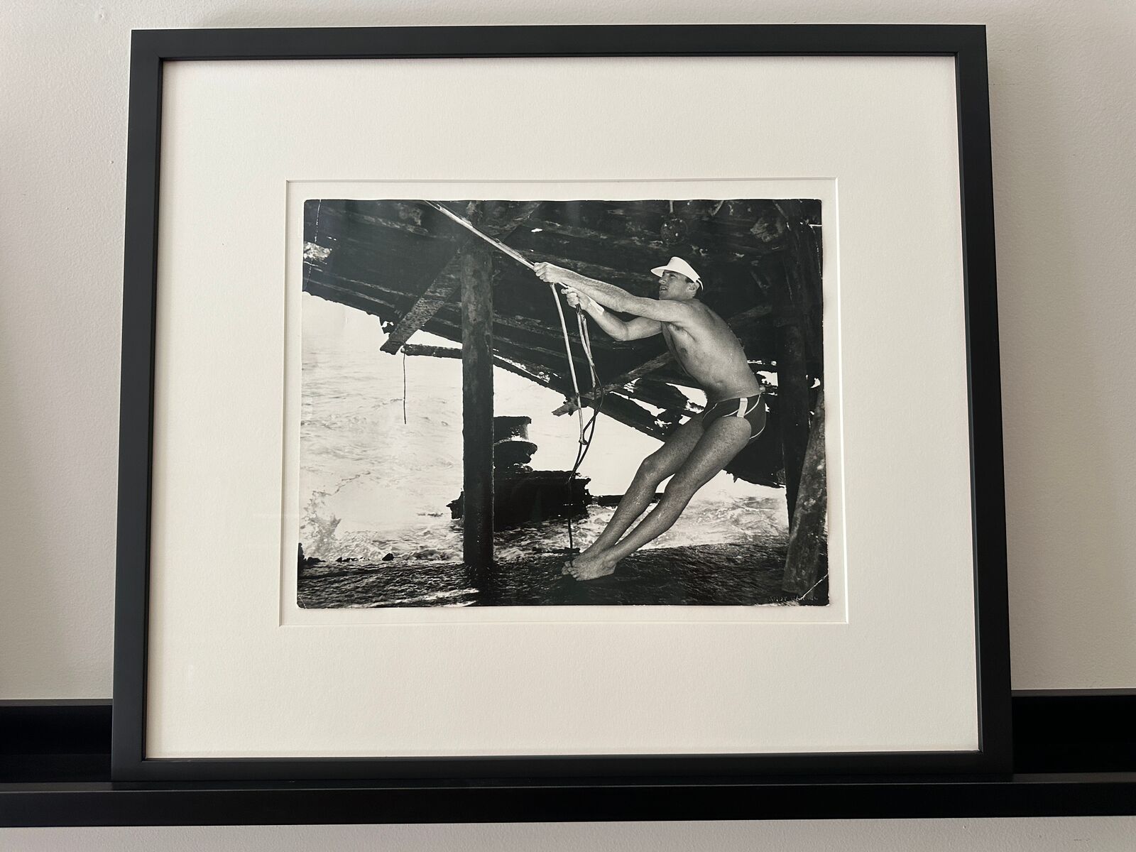 A man in a bathing suit and hat holding onto a rope.