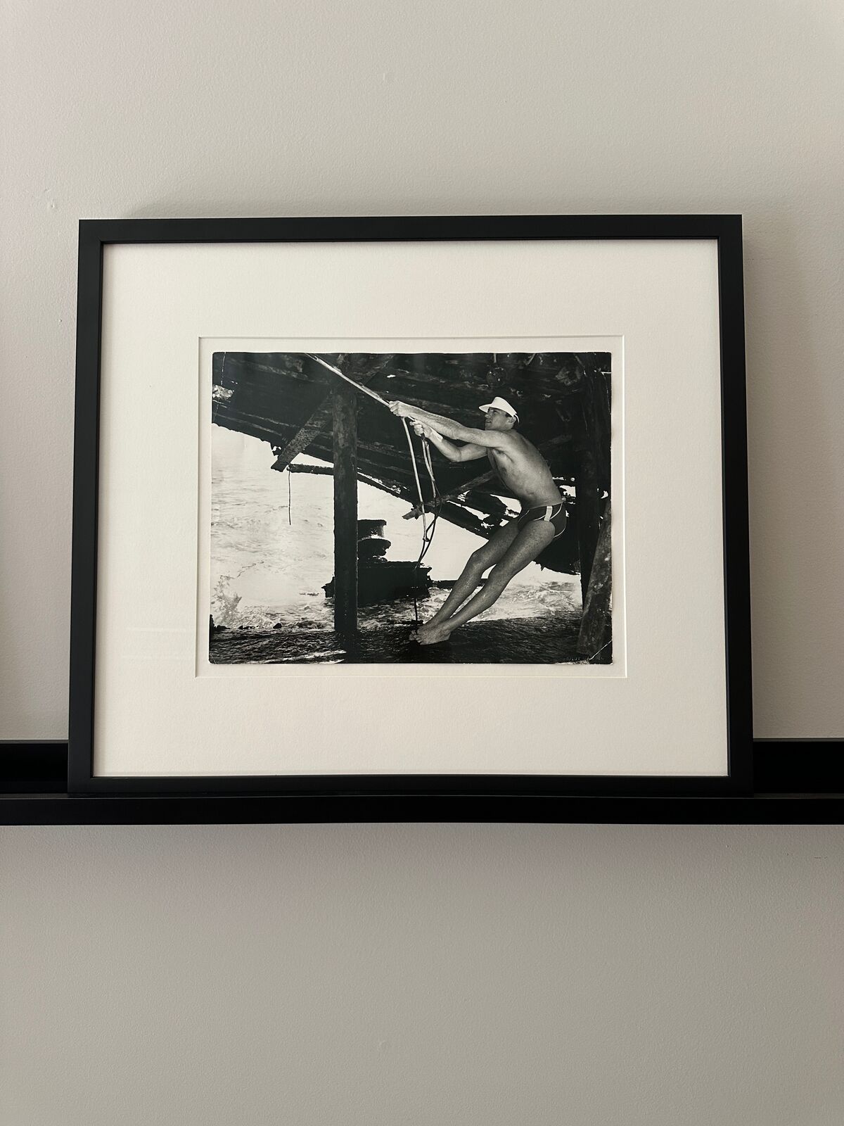 A man in a bathing suit and hat holding onto a rope.