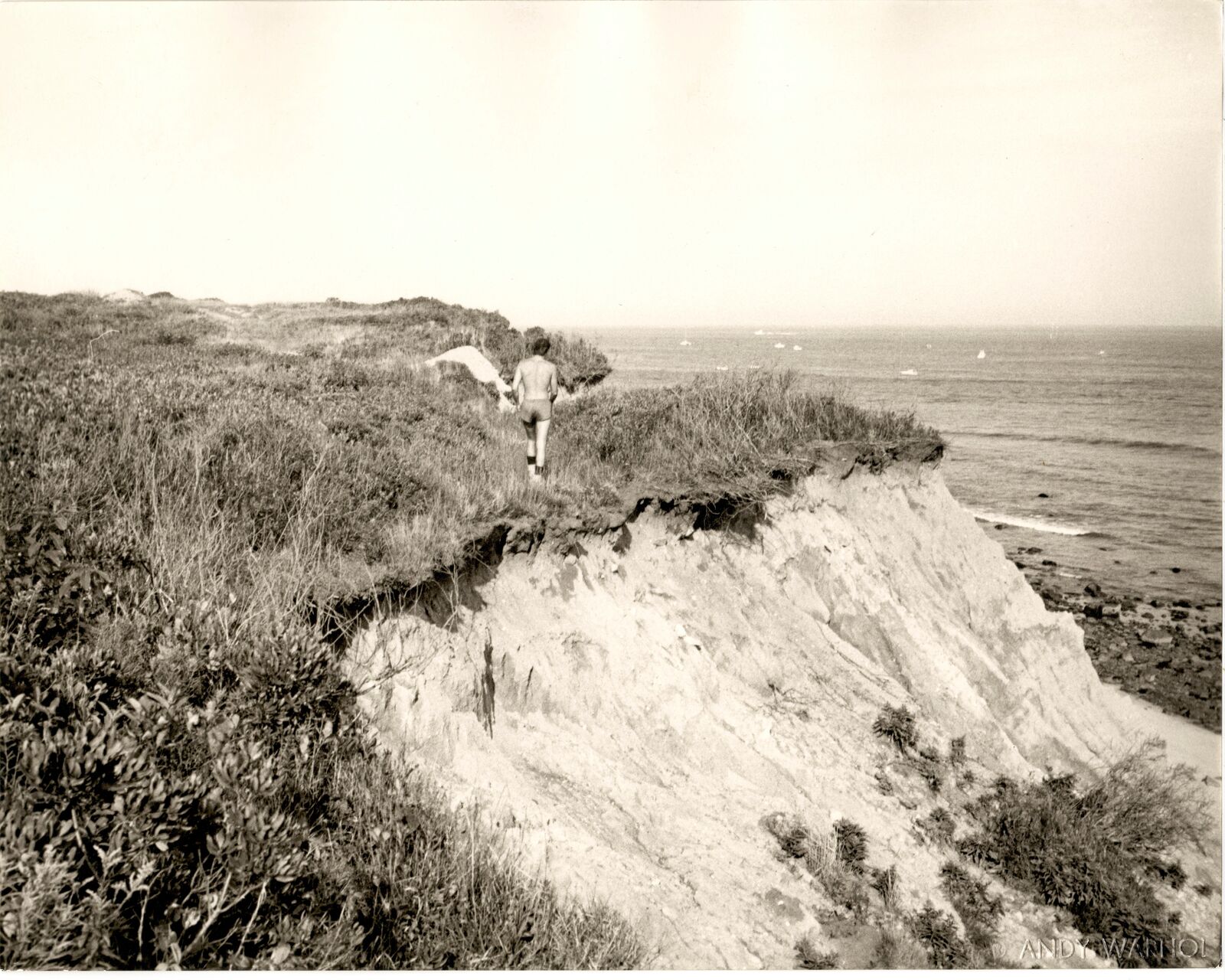 A black and white photo of a man walking on a cliff.
