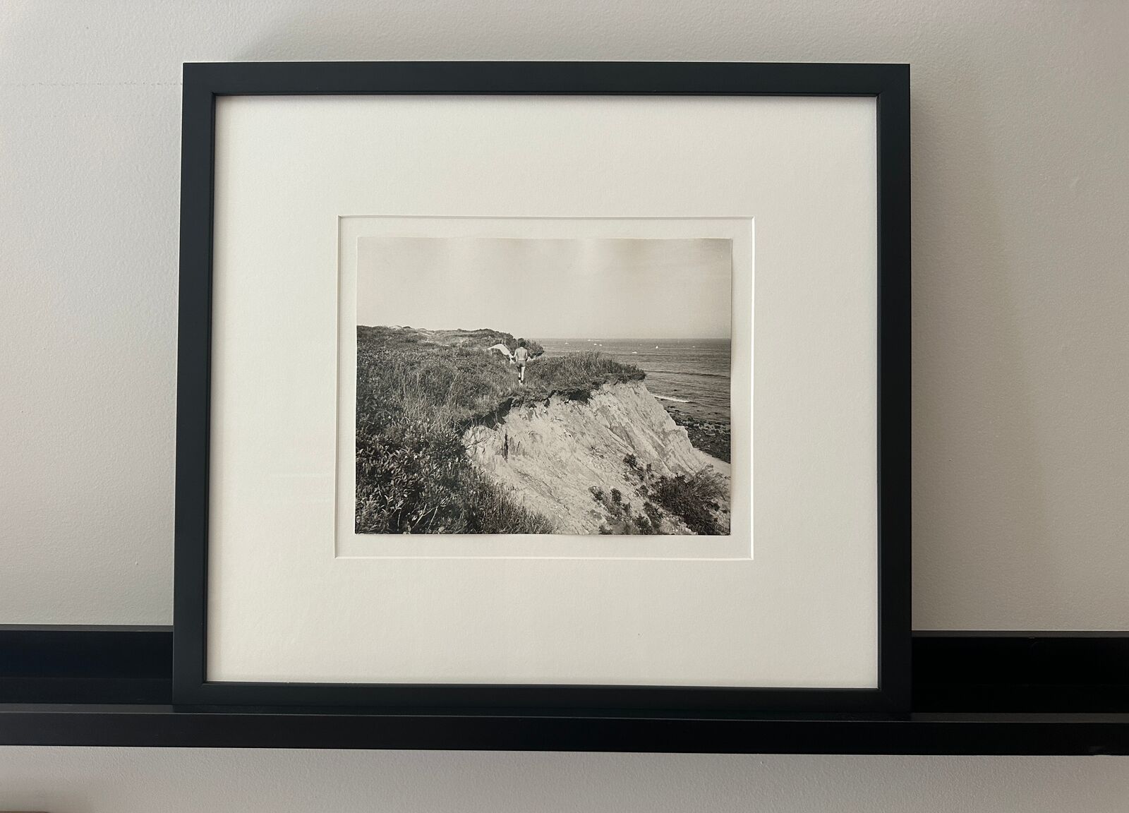 A black and white photo of a man walking on a cliff.