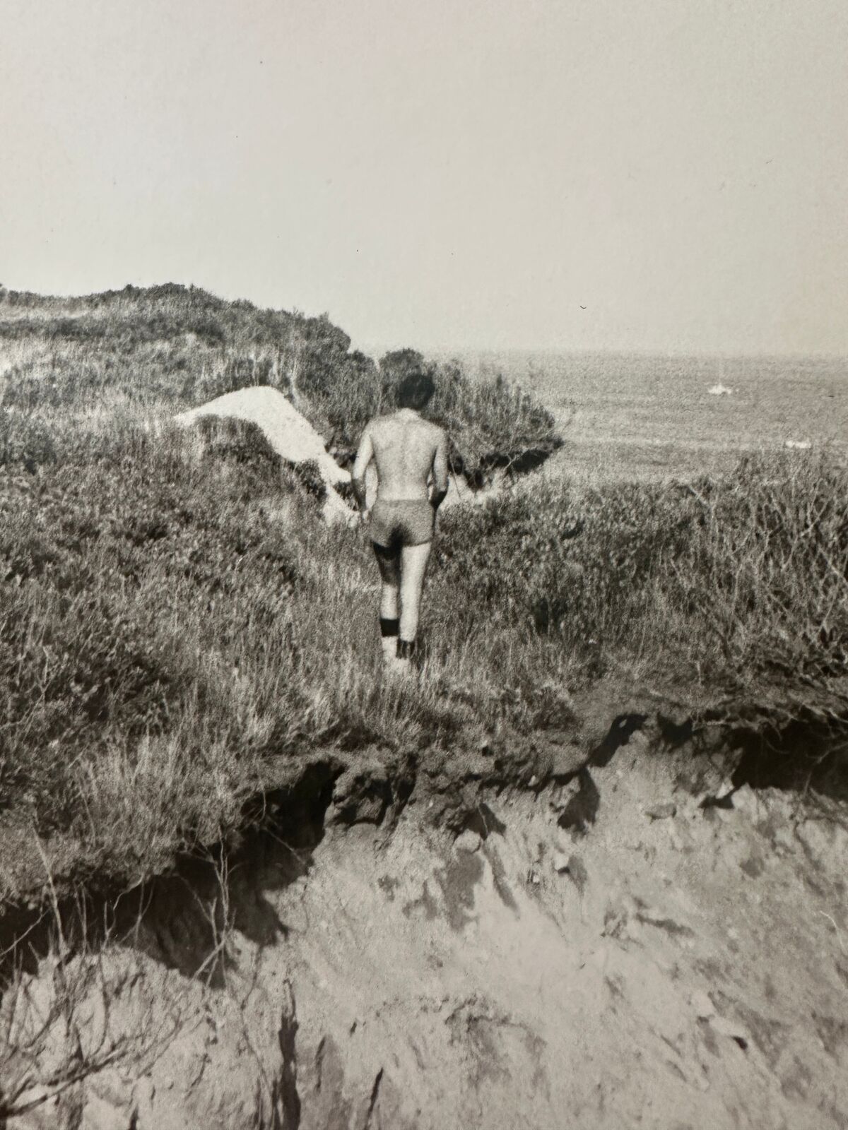 A black and white photo of a man walking on a cliff.