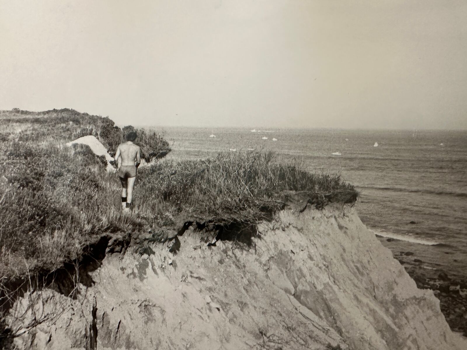 A black and white photo of a man walking on a cliff.