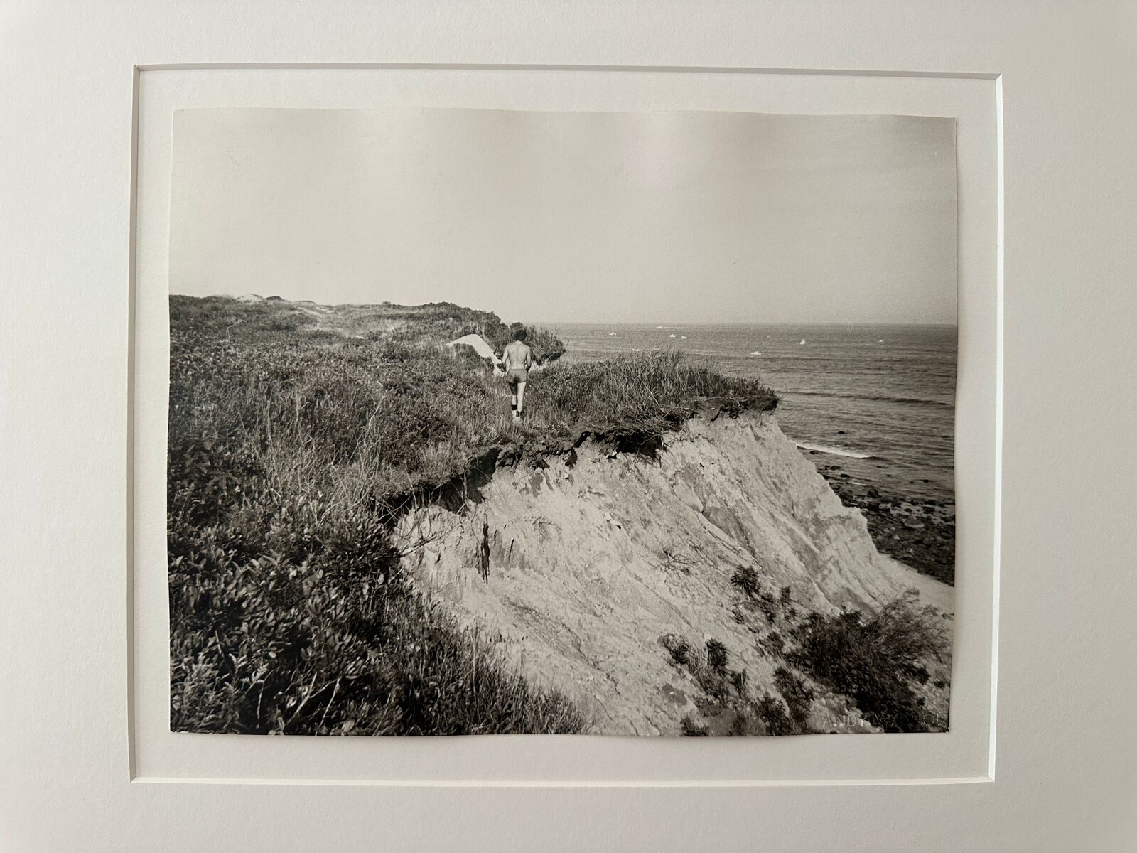 A black and white photo of a man walking on a cliff.