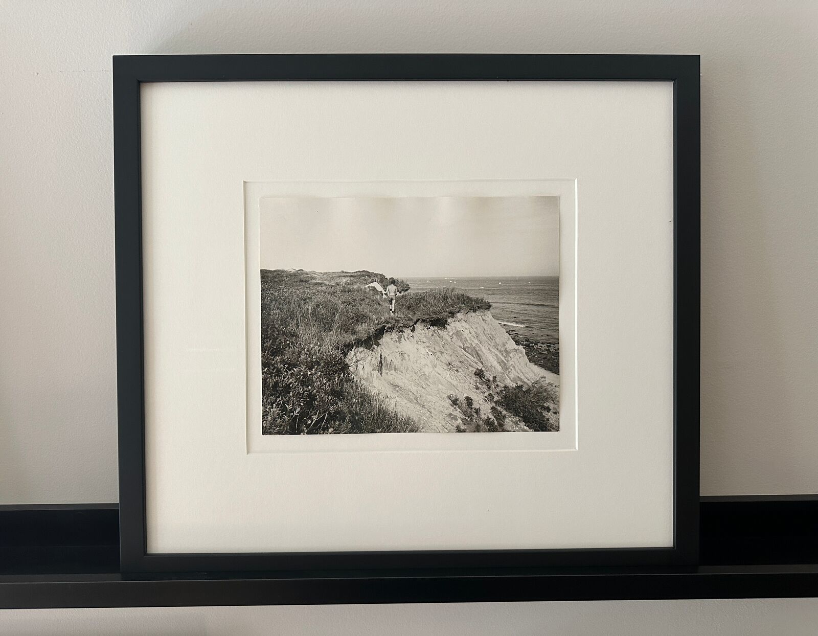 A black and white photo of a man walking on a cliff.