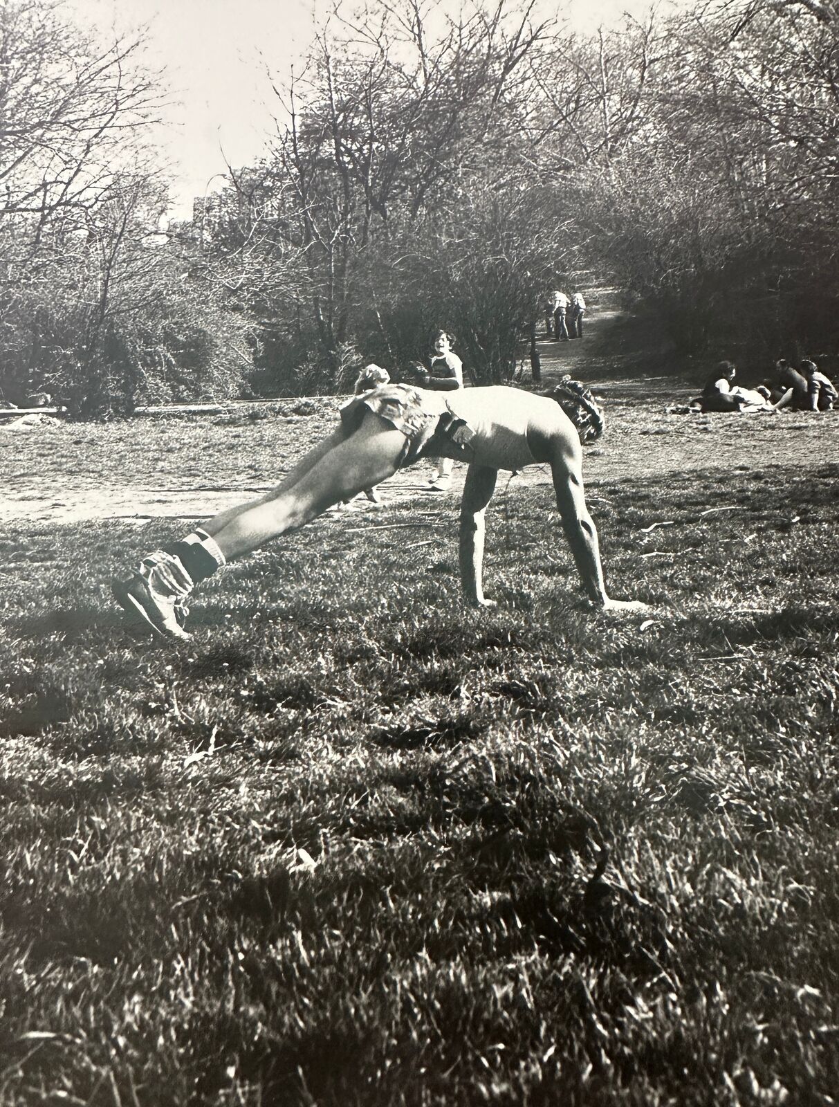 A black and white photo of a man doing a handstand in a park.