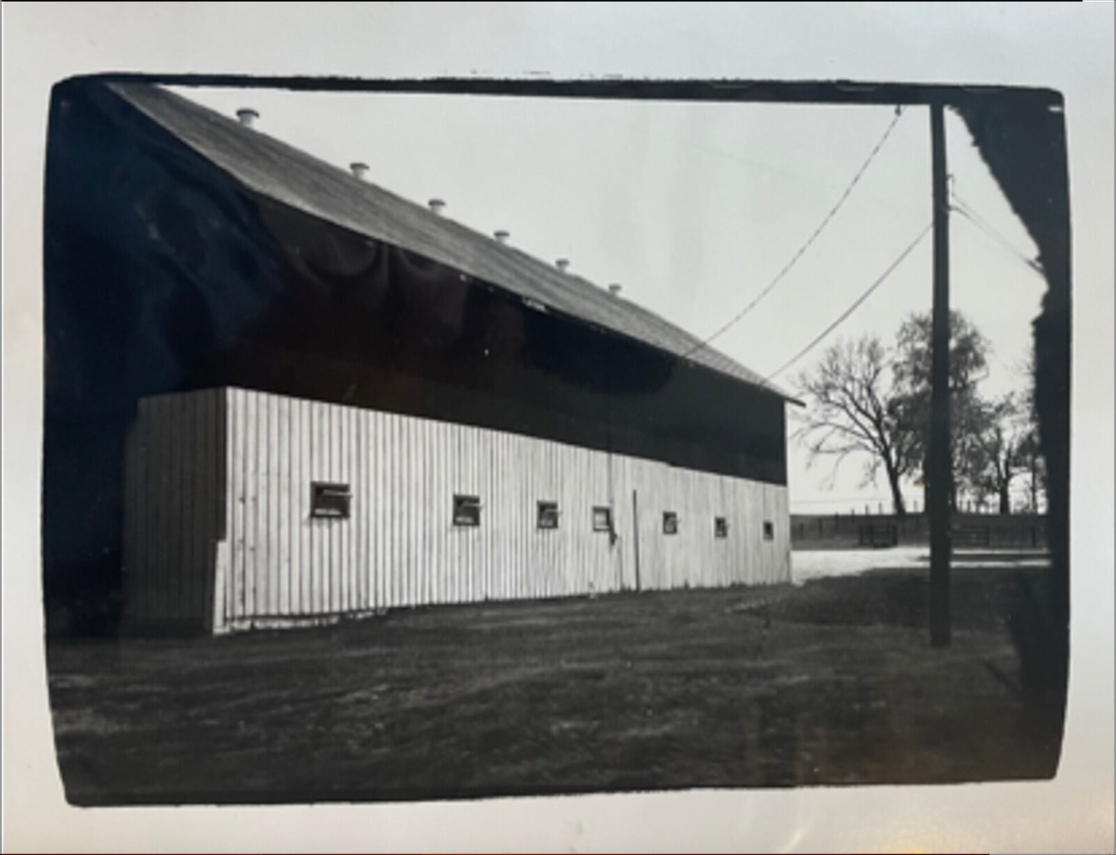 A black and white photo of a barn in a field.