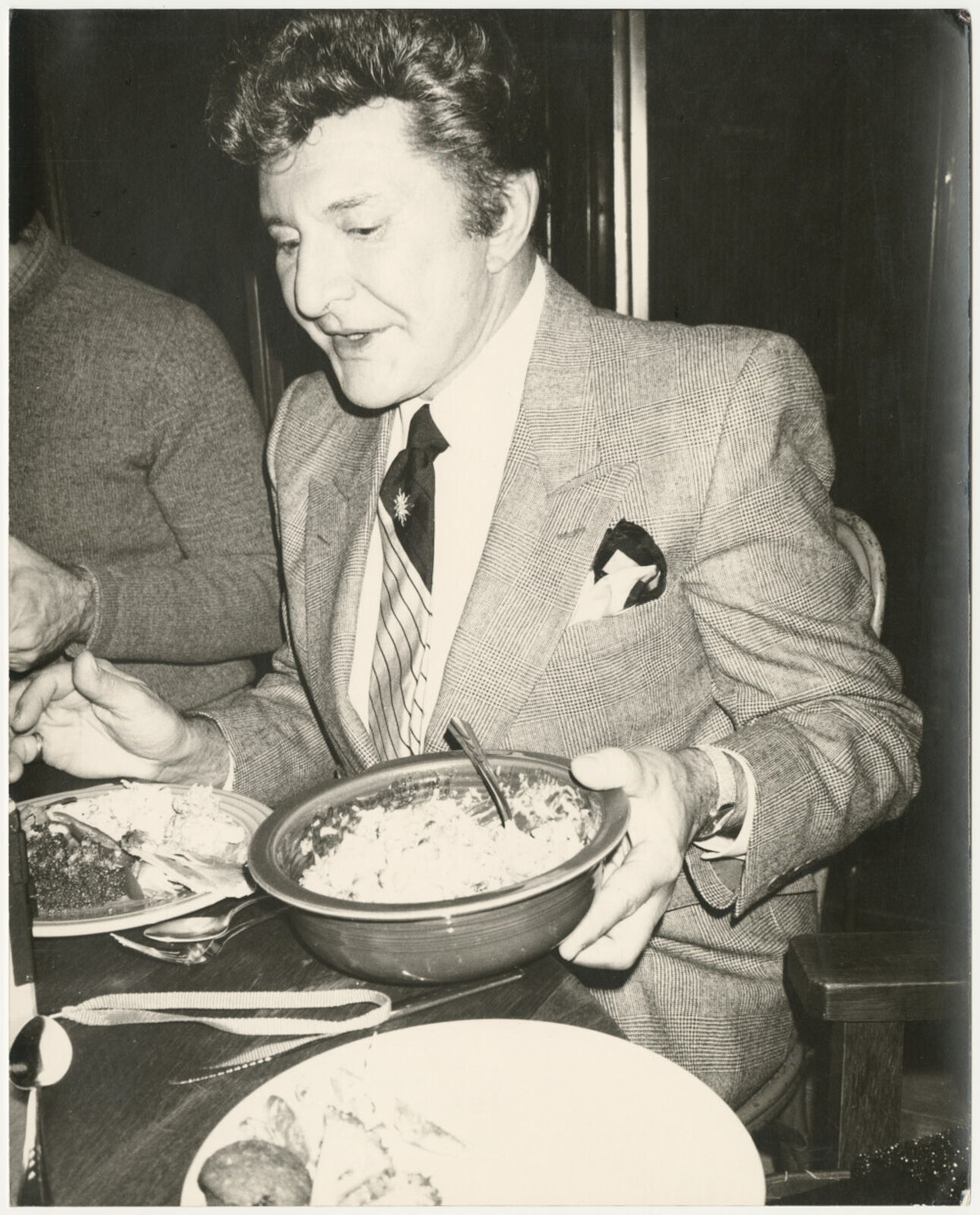 A man in a suit sitting at a table with a bowl of food.