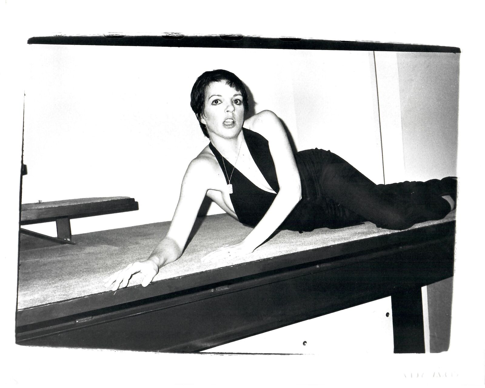 A black and white photo of a woman laying on a pool table.