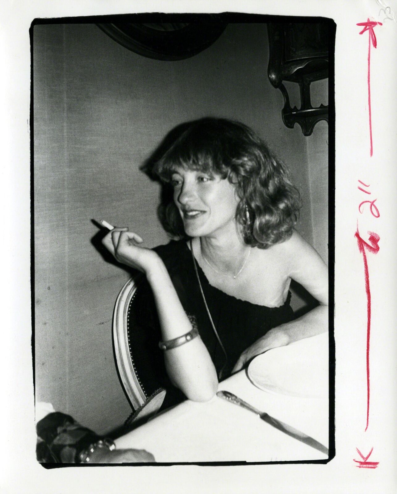 A black and white photo of a woman sitting at a table smoking a cigarette.