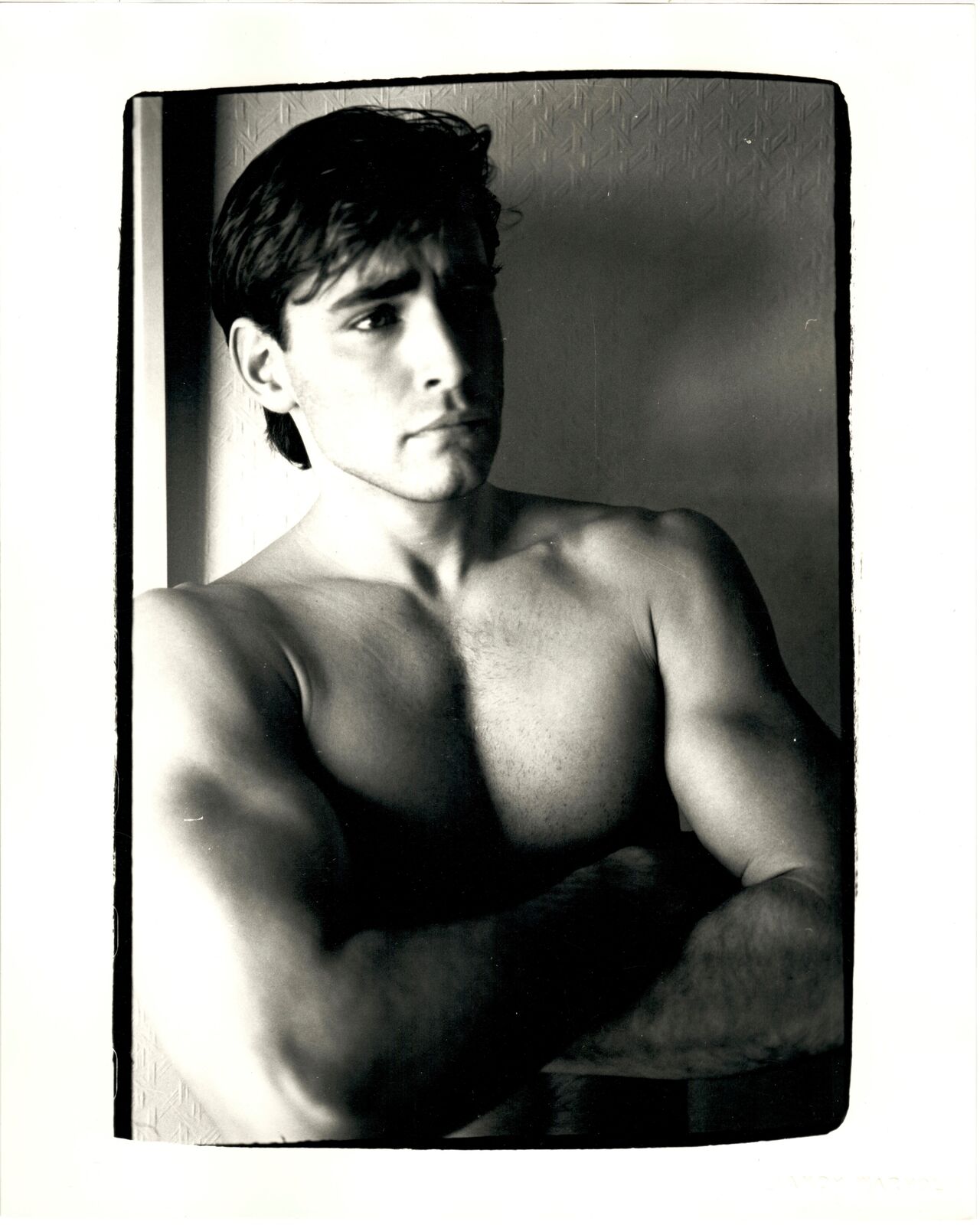 A black and white photo of a shirtless man with his arms crossed.