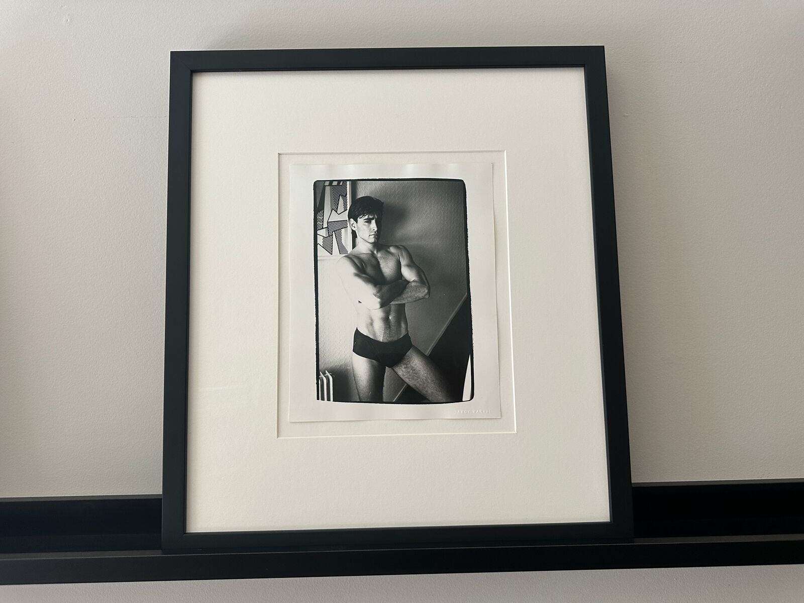 A shirtless man in a black underwear leaning against a wall.