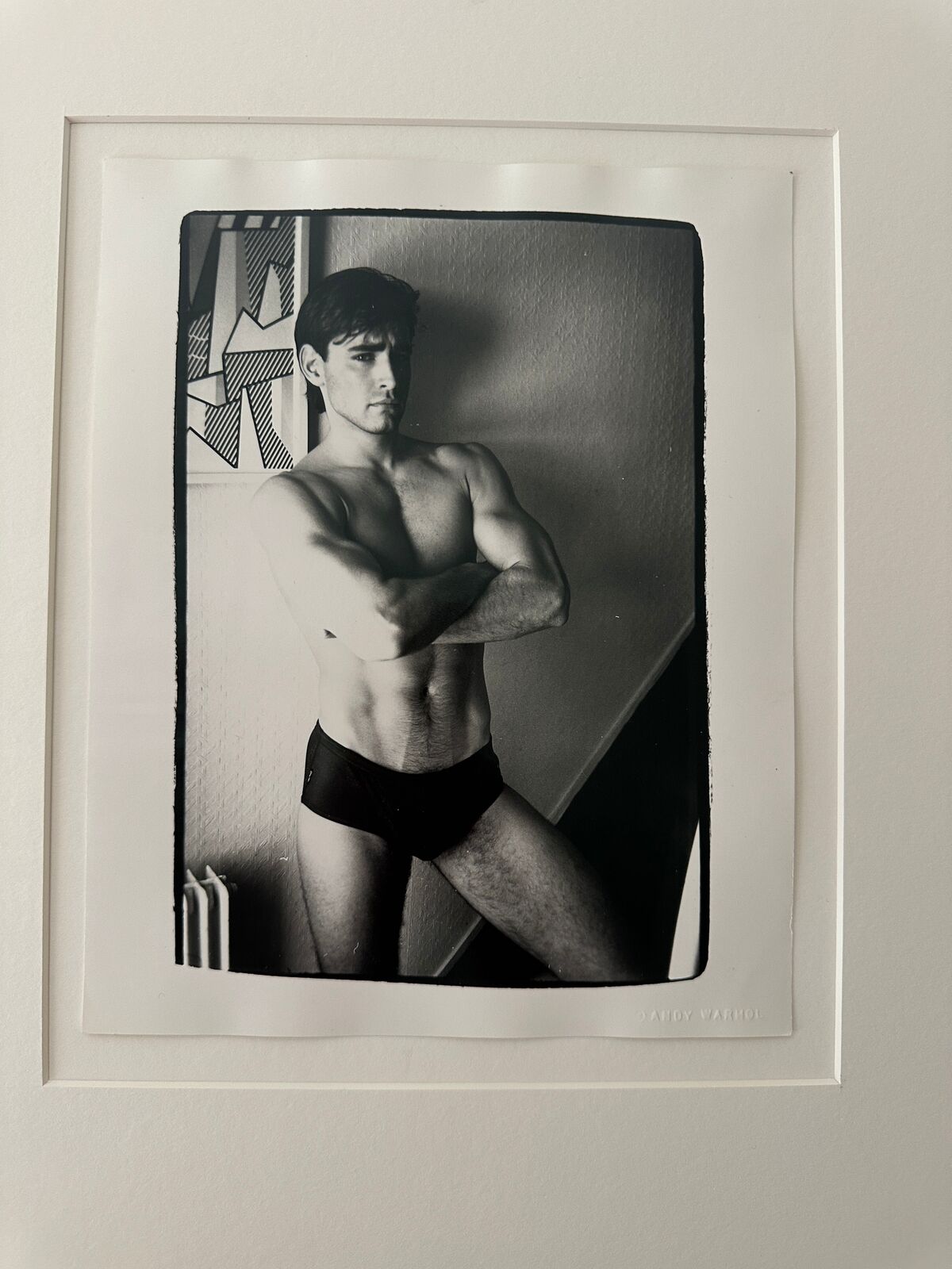 A shirtless man in a black underwear leaning against a wall.