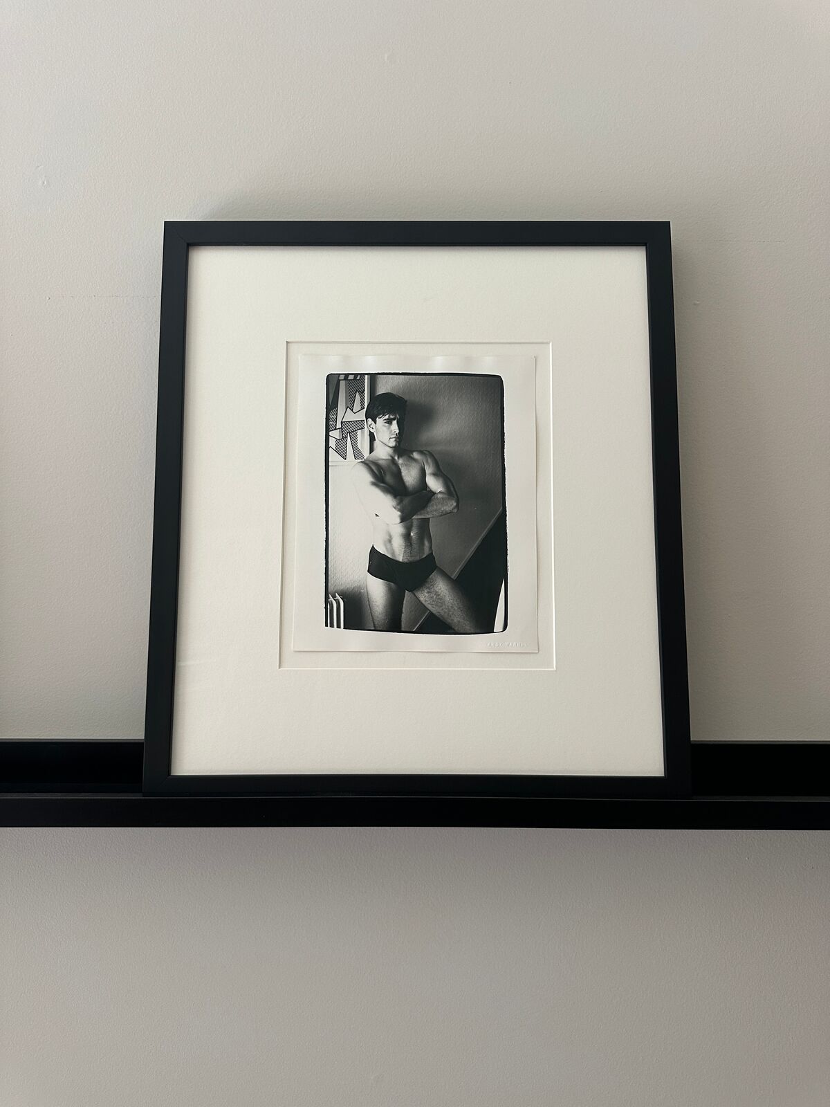 A shirtless man in a black underwear leaning against a wall.