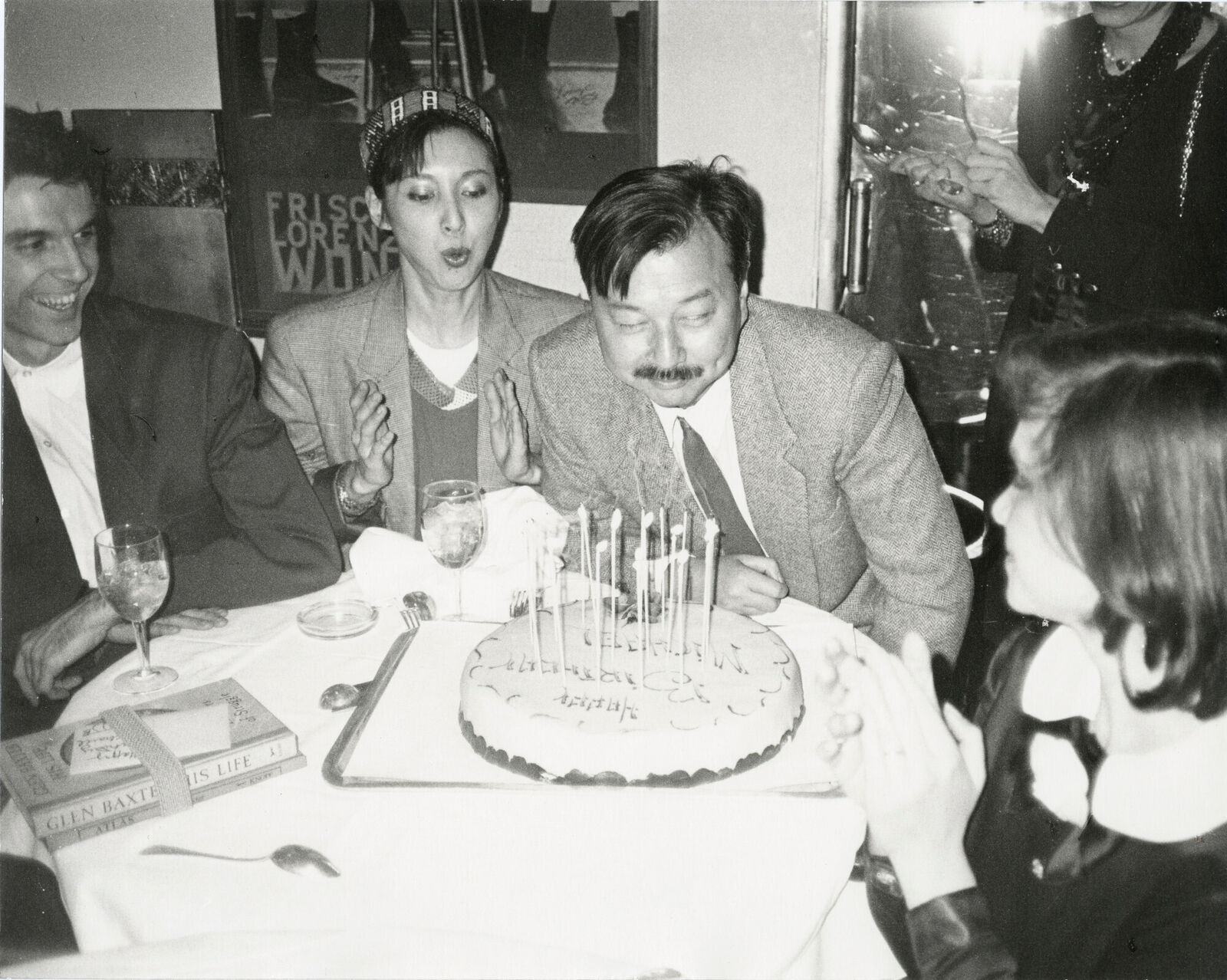A group of people sitting around a table with a birthday cake.