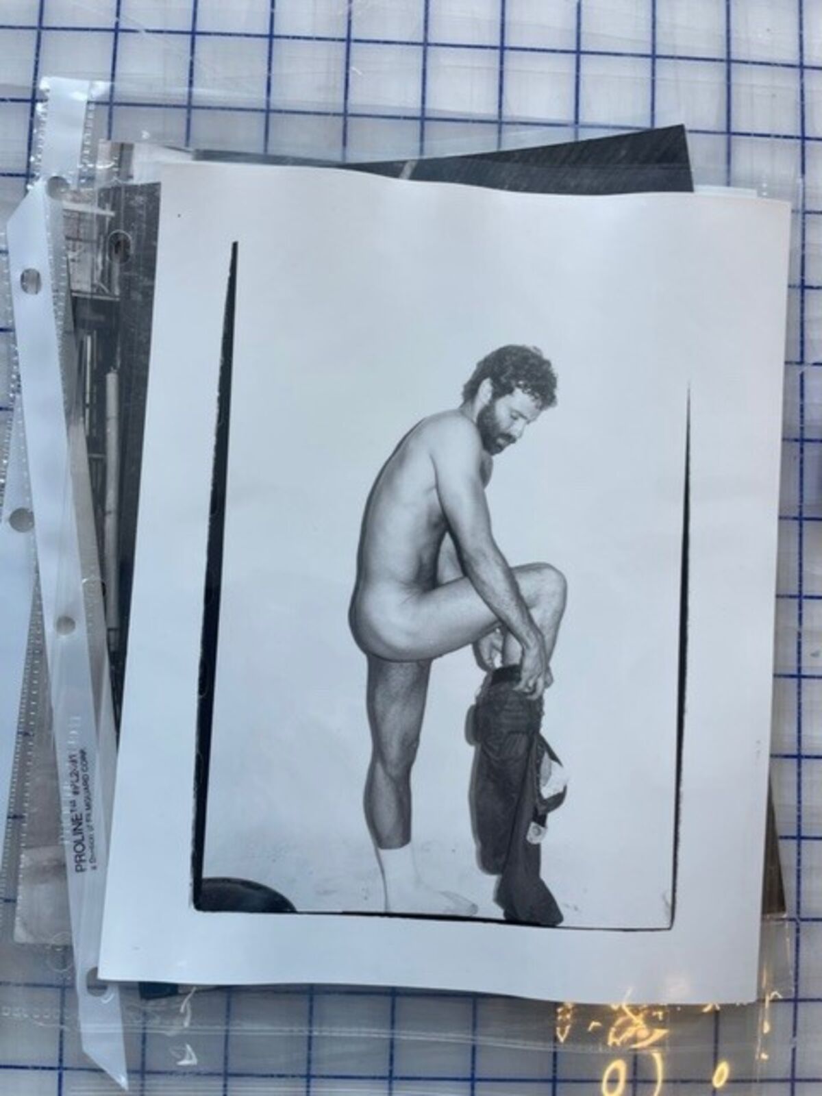 A black and white photo of a naked man kneeling on the ground.