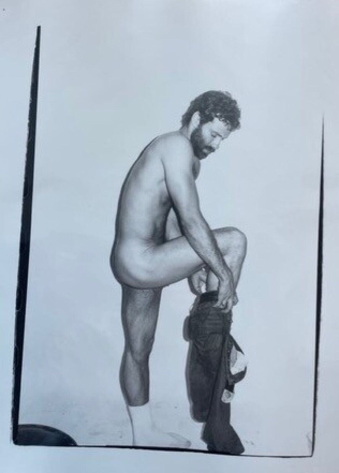 A black and white photo of a naked man kneeling on the ground.