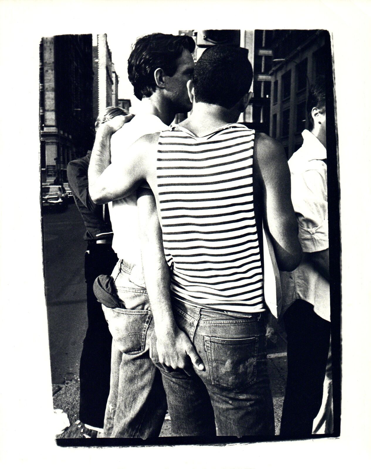 A black and white photo of two men kissing on the street.
