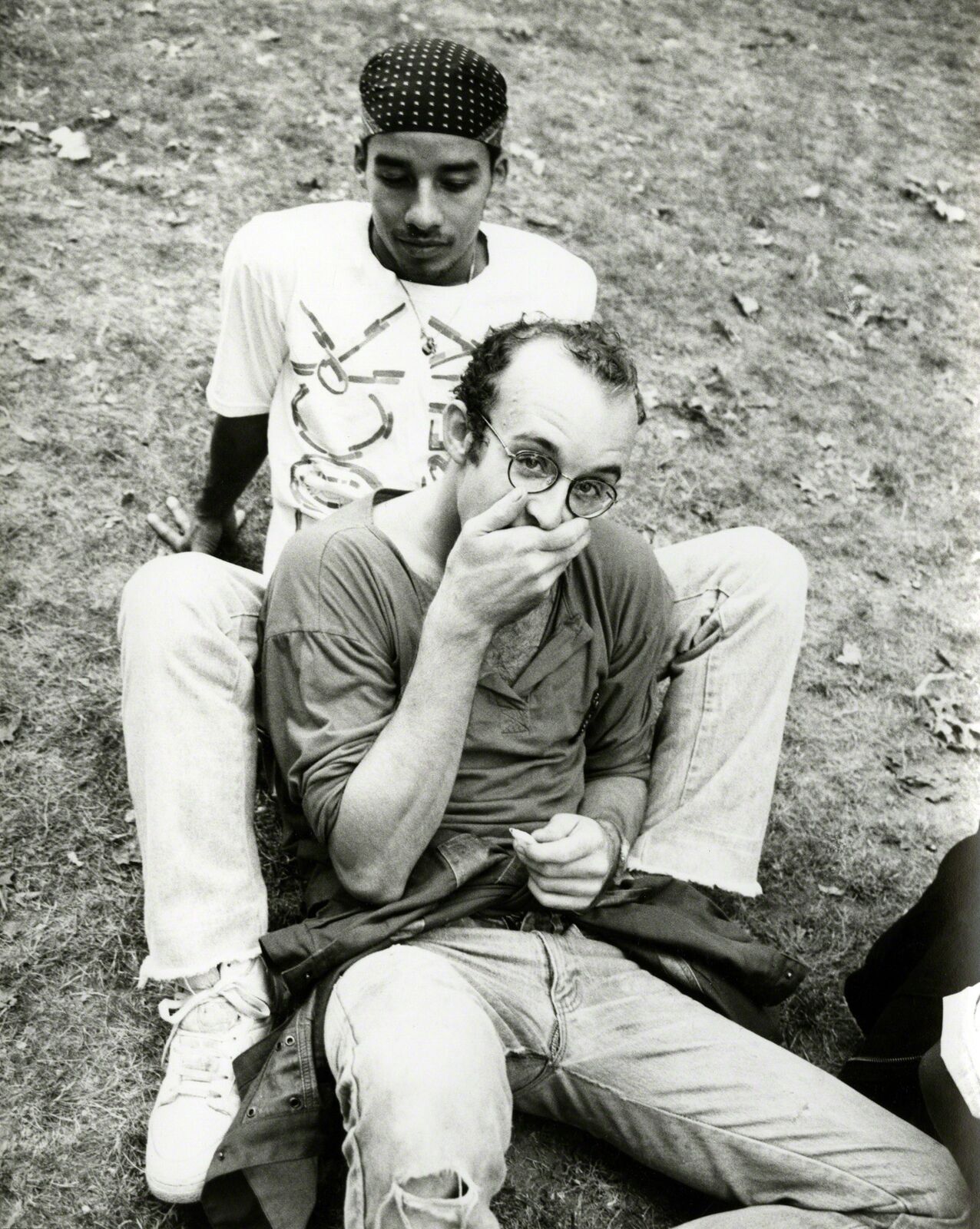 A man sitting on the ground next to another man smoking a cigarette.