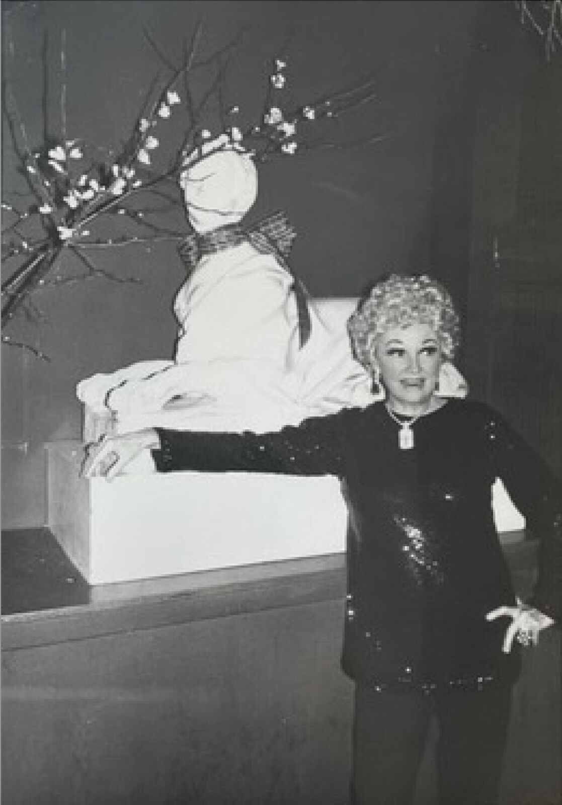 A black and white photo of a woman standing next to a snowman.