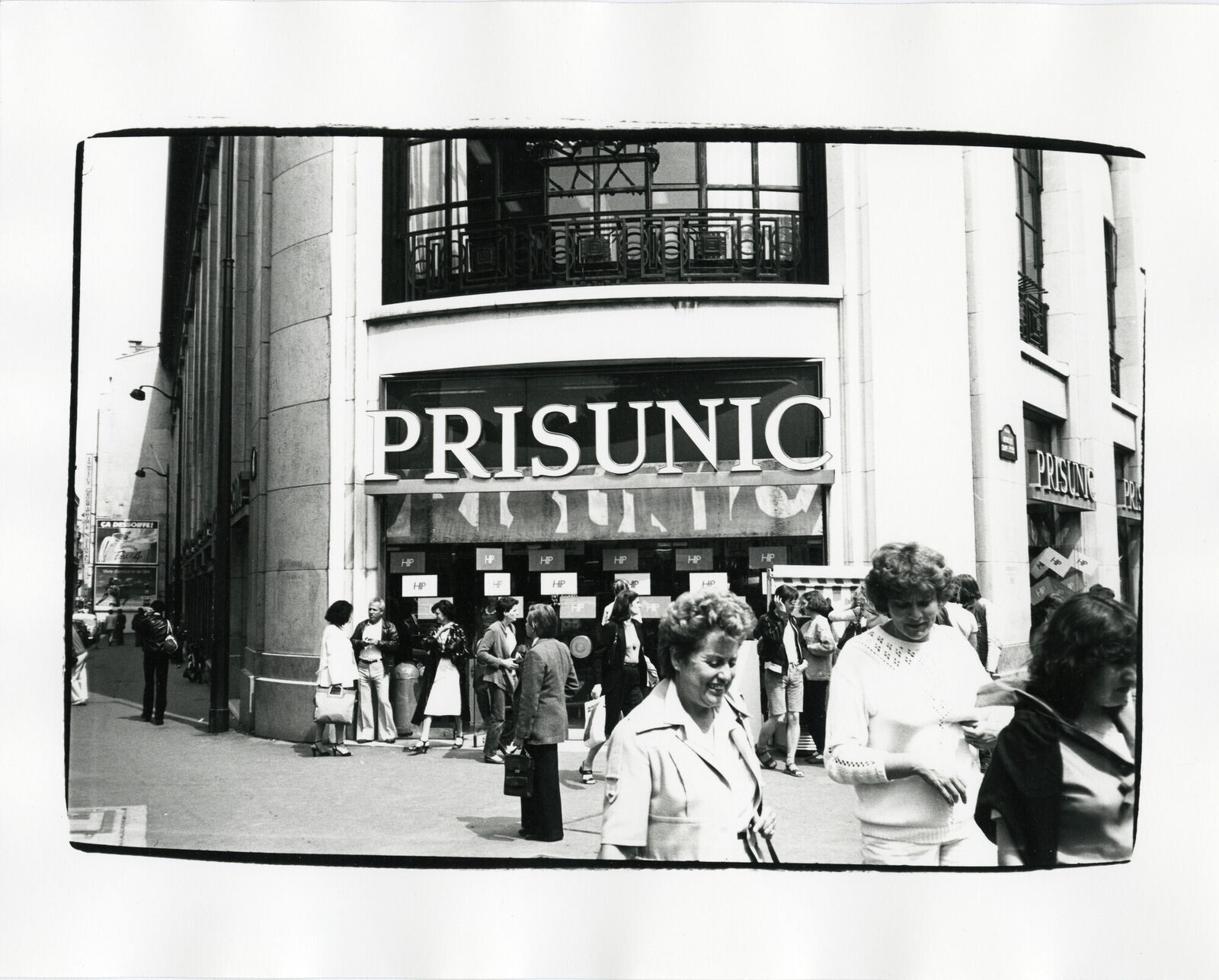A black and white photo of people walking in front of a store.