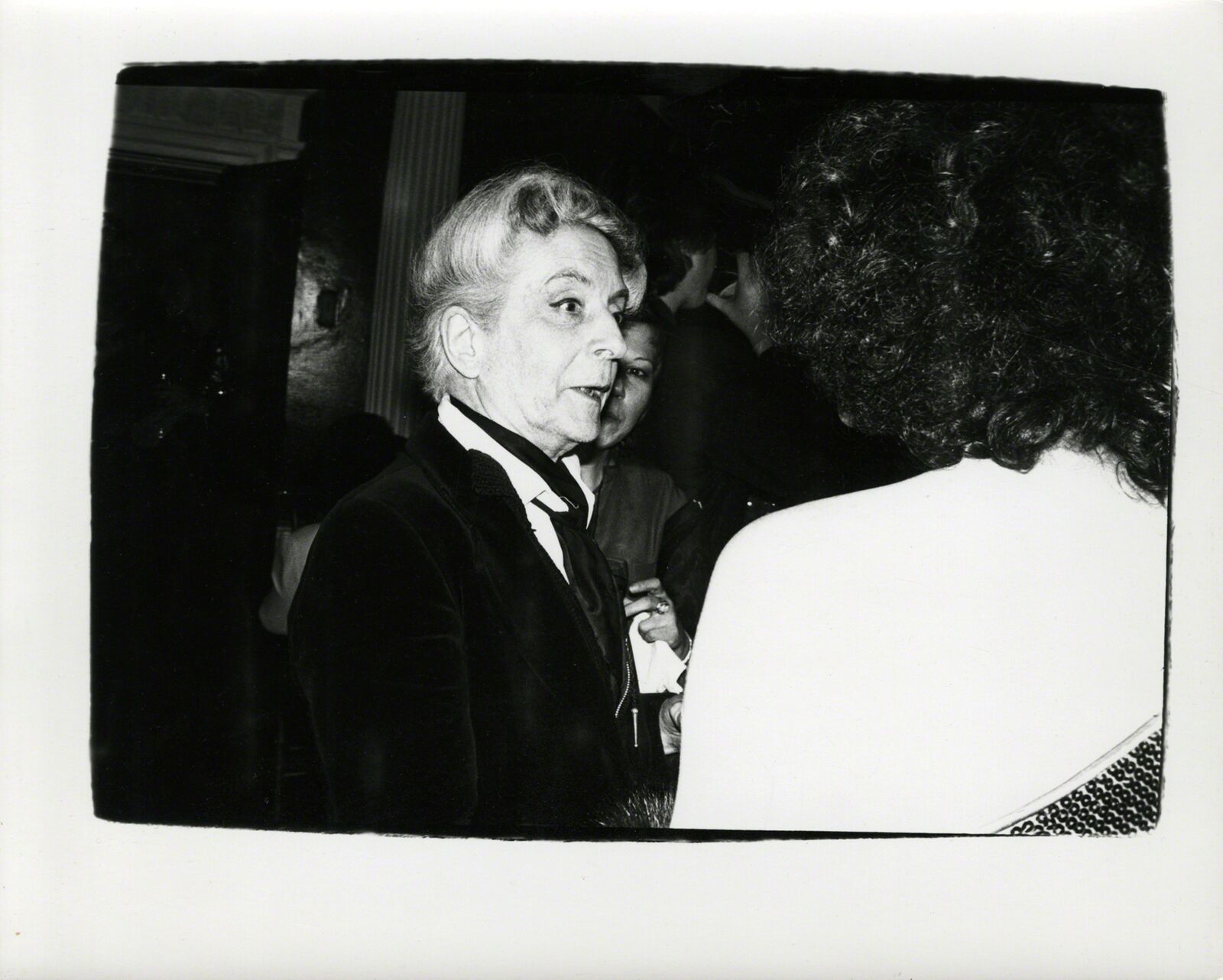 A black and white photo of a man in a tuxedo talking to a woman.