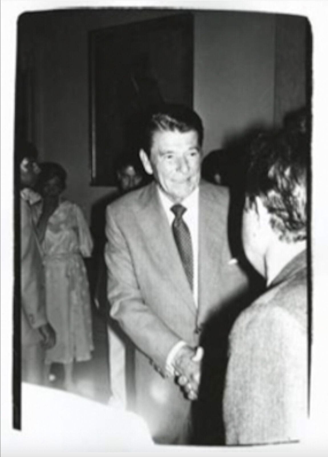 A black and white photo of a man in a suit shaking hands with another man.
