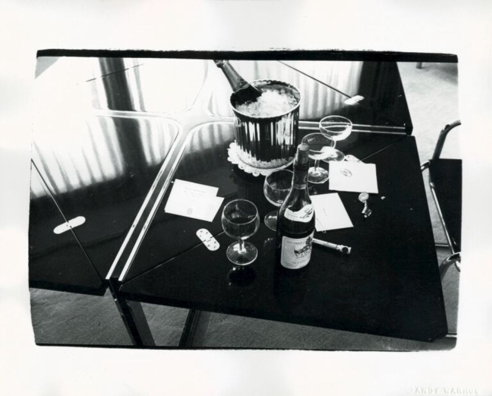 A black and white photo of a table with wine glasses and a bottle of wine.