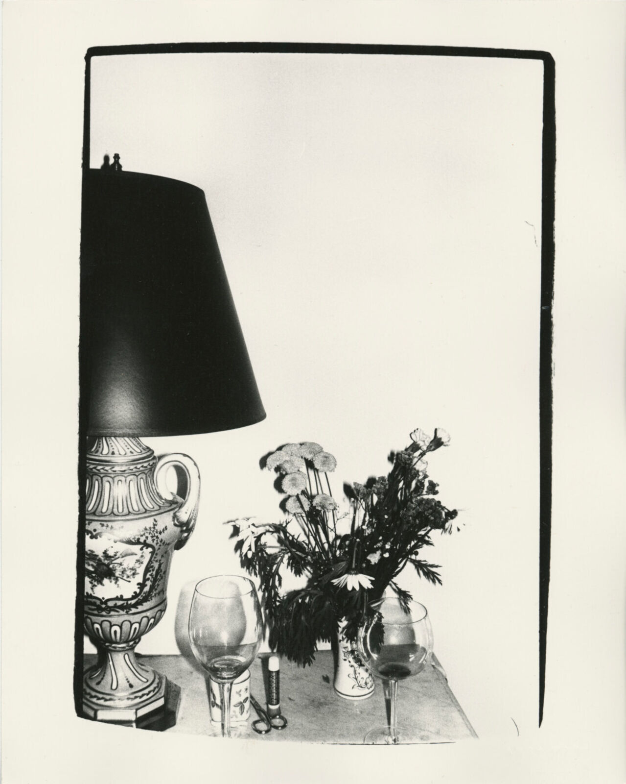 A black and white photo of a table with a lamp and a vase of flowers.
