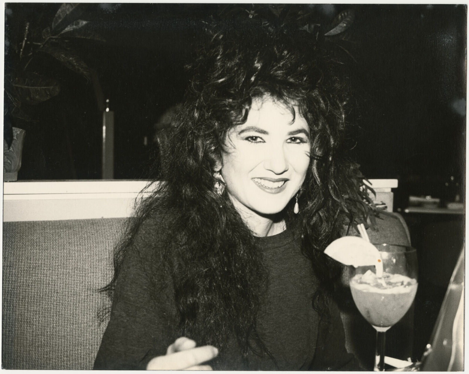 A black and white photo of a woman sitting at a table with a drink.