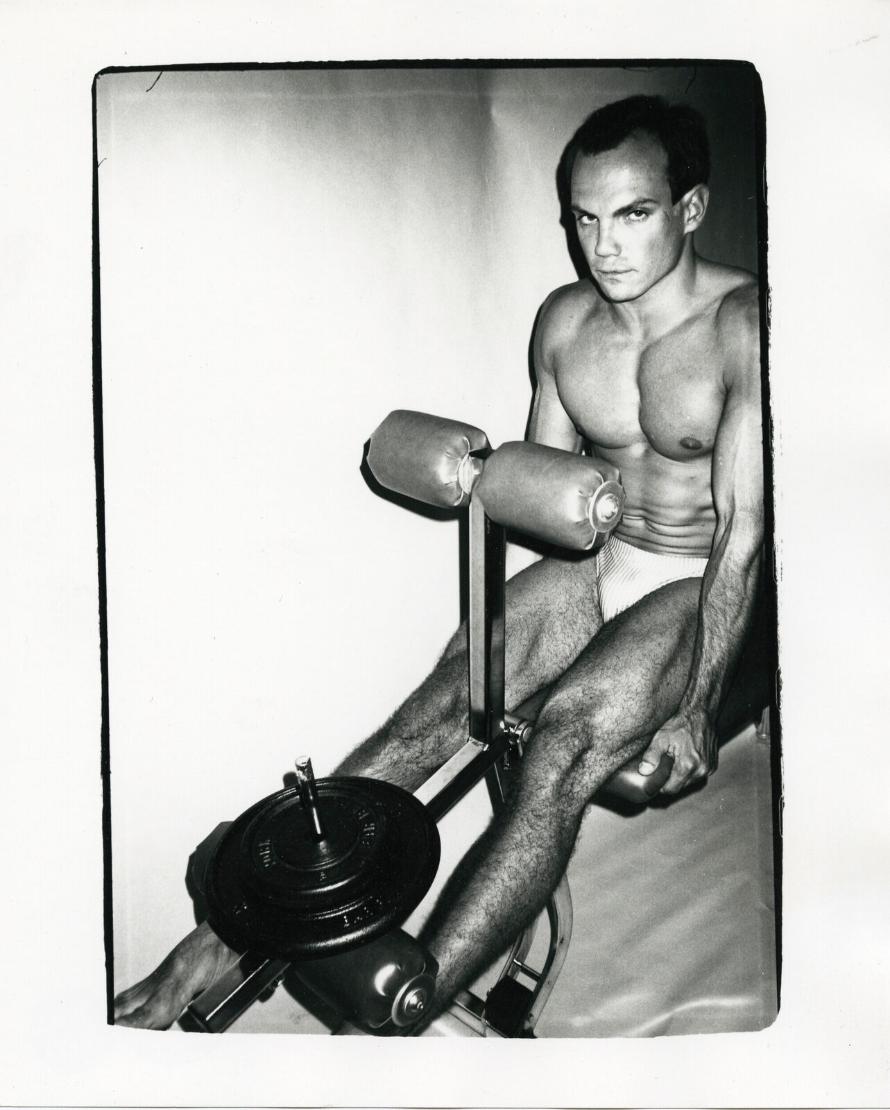 A black and white photo of a man sitting on a gym machine.