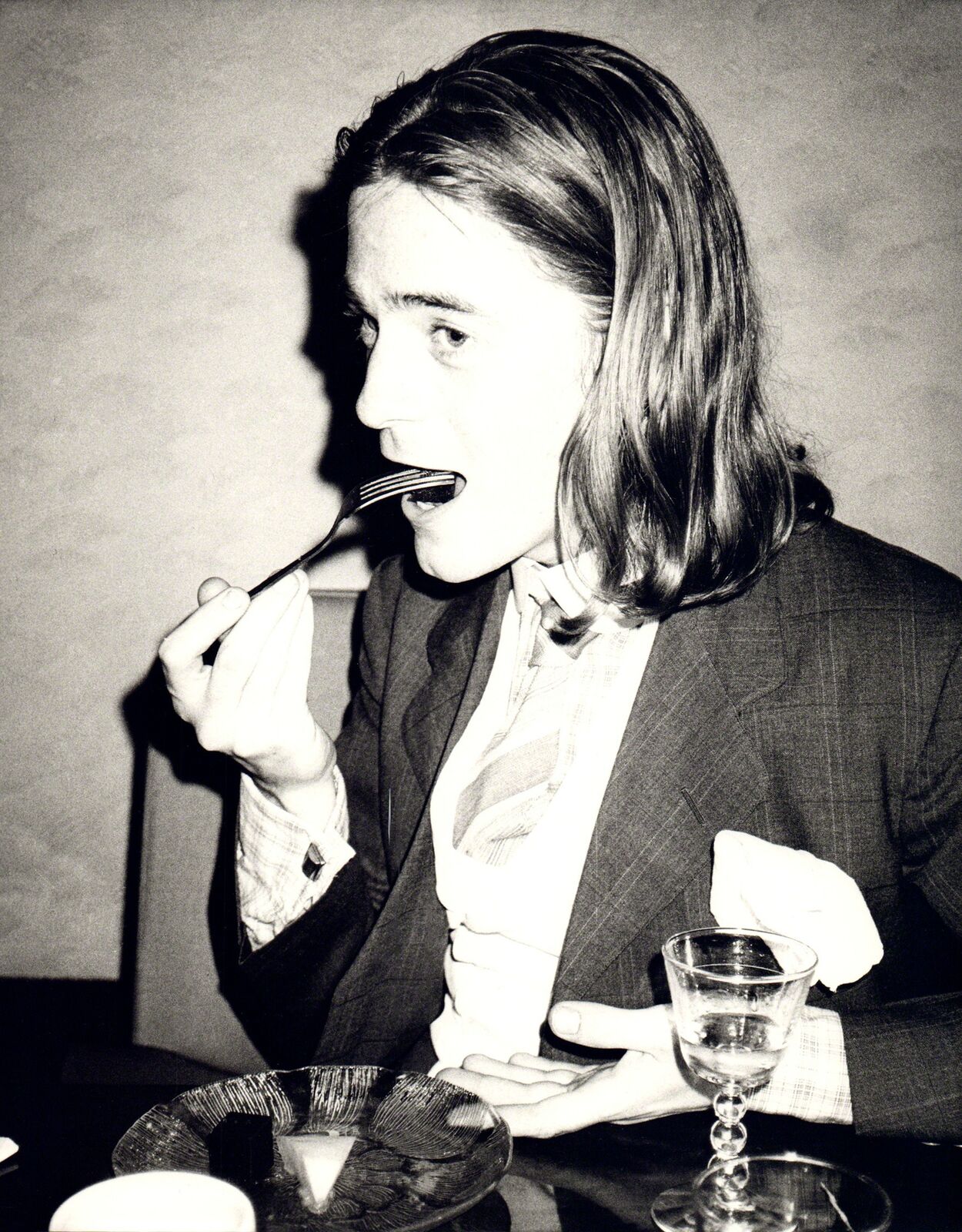 A woman sitting at a table with a fork in her mouth.