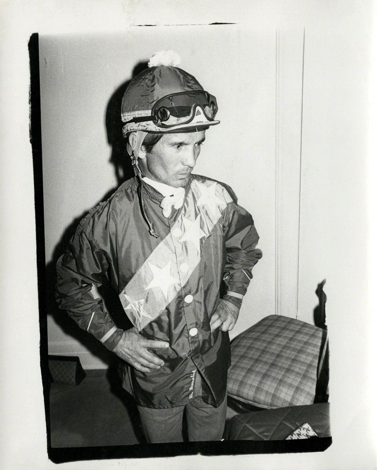 A black and white photo of a jockey wearing a hat and goggles.