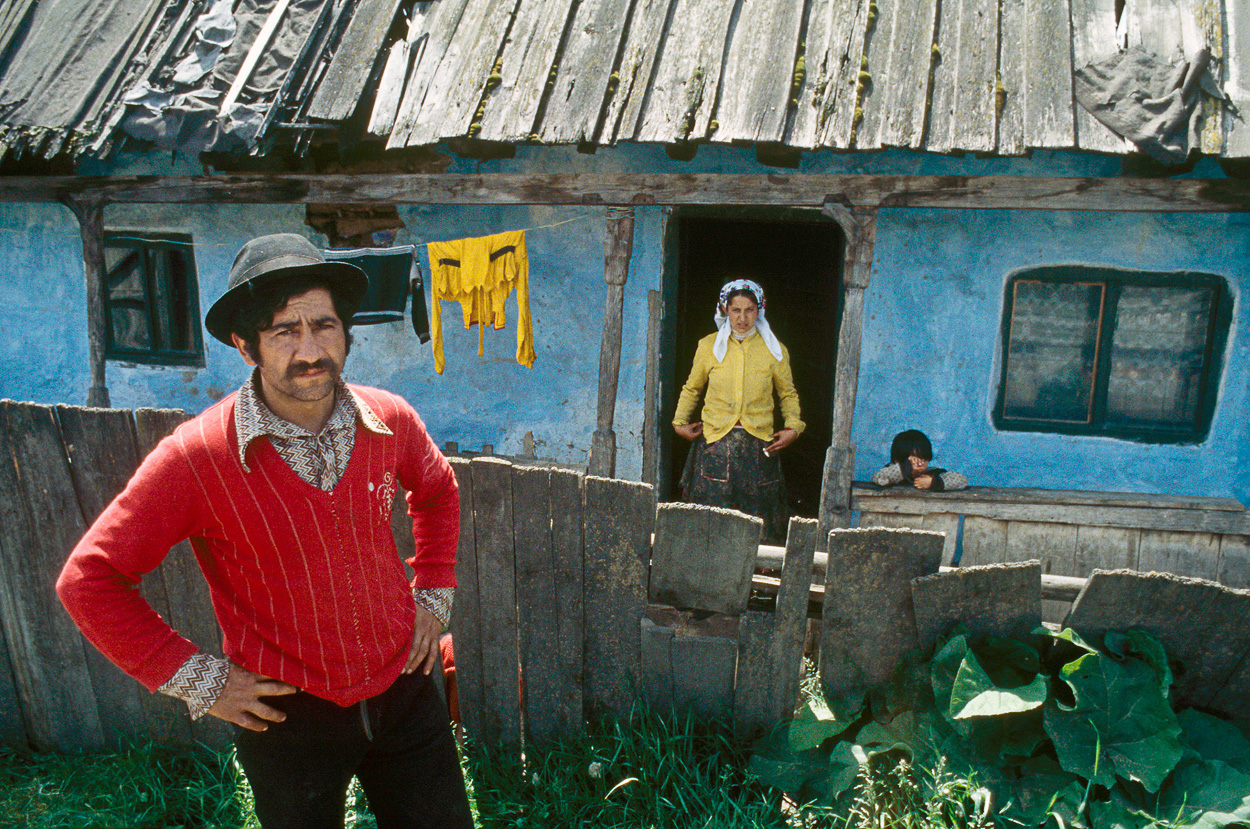 A man standing in front of a blue house with clothes hanging out to dry.