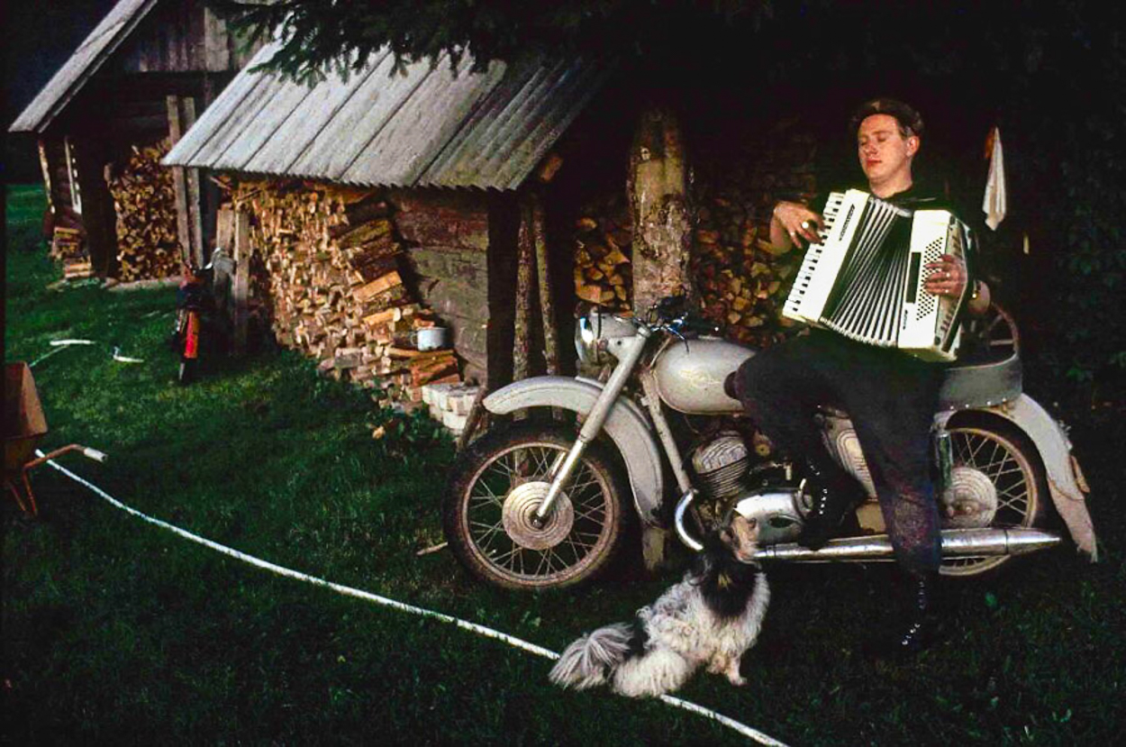 A man playing an accordion on a motorcycle next to a dog.
