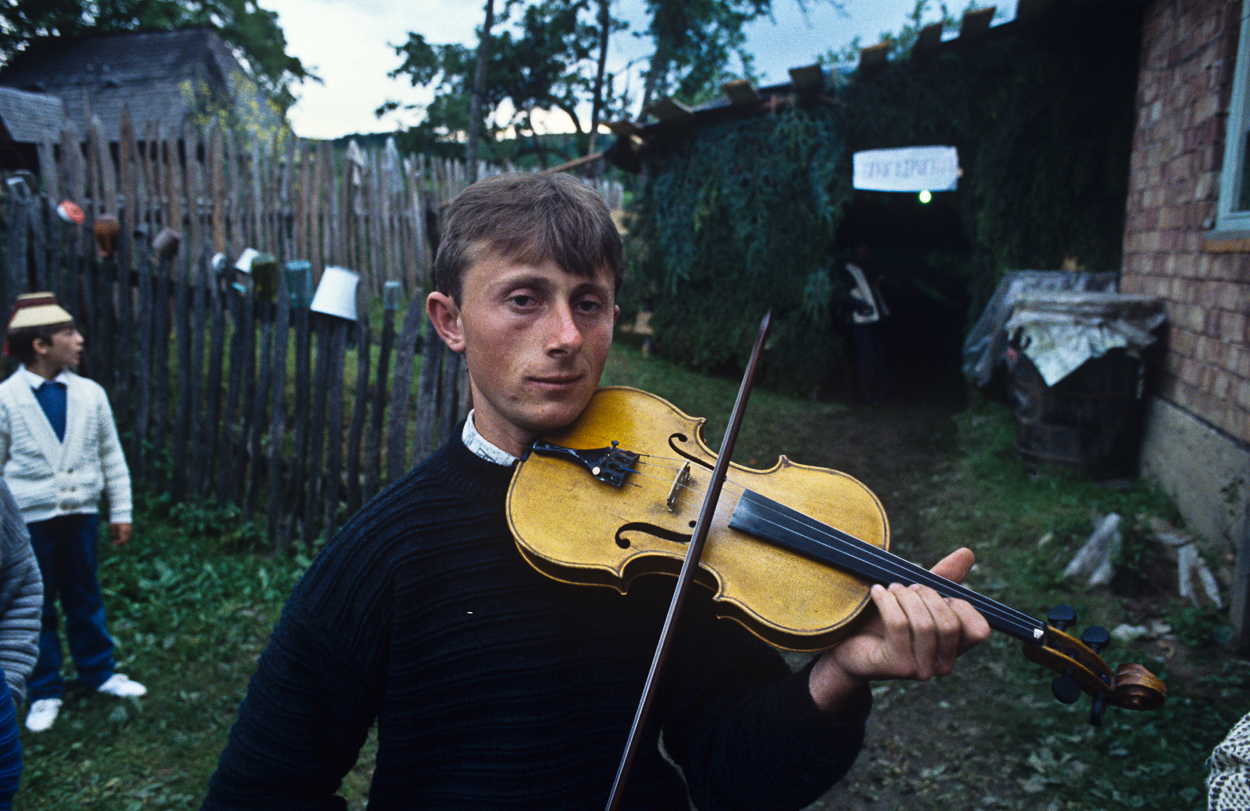 A man holding a violin in front of a house.