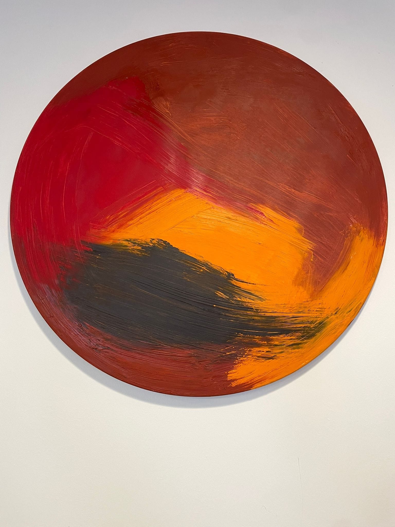 A bold abstract painting featuring a large circle with sweeping brushstrokes in red, orange, and black.
