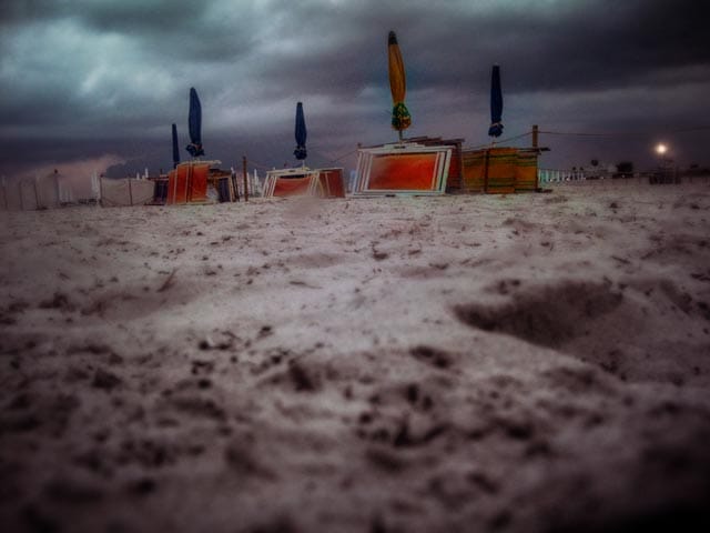 A low-angle view of a deserted beach with closed umbrellas under a heavy, dark sky.