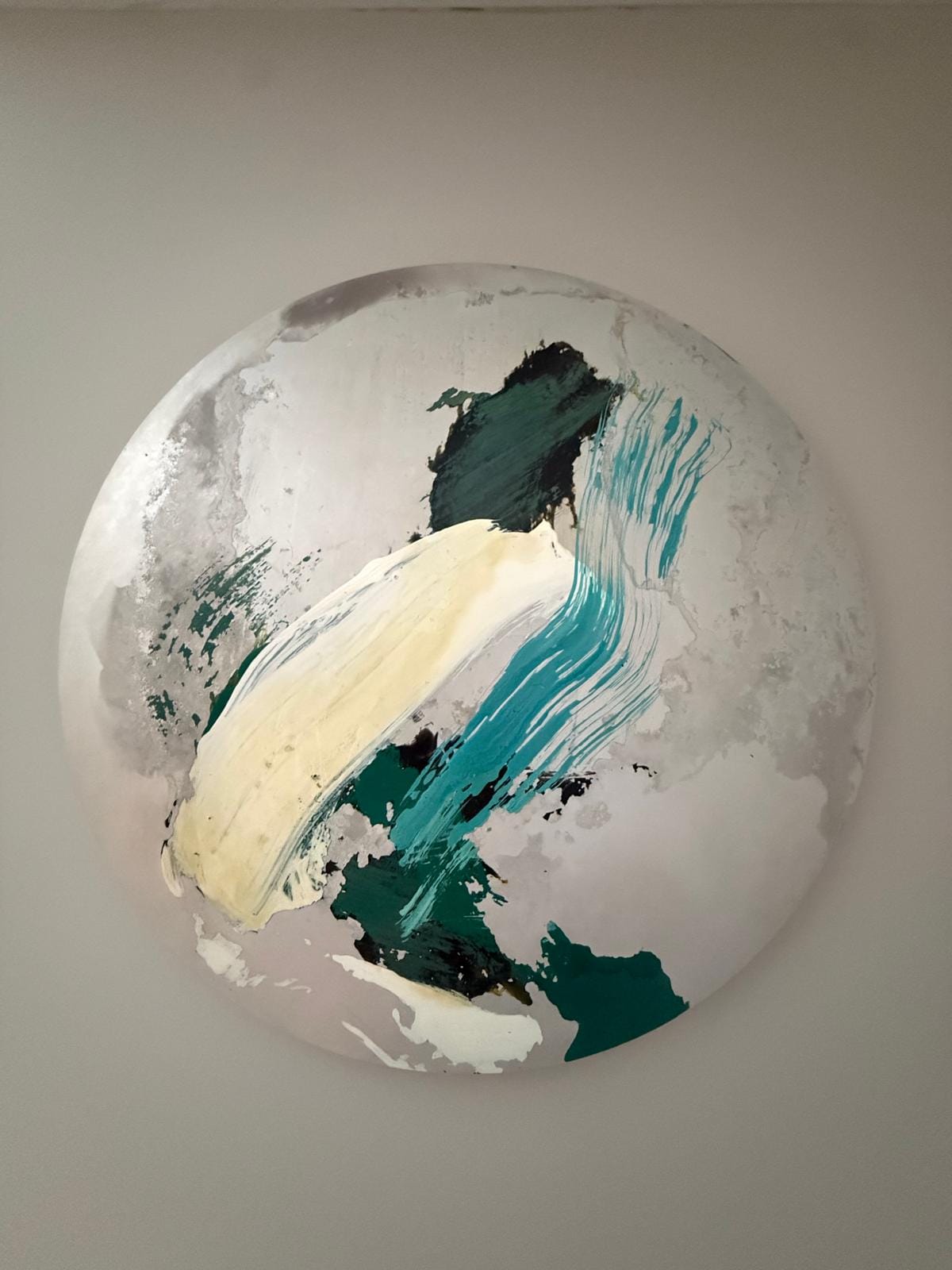 A circular abstract painting featuring bold, expressive brushstrokes in teal, cream, and dark green against a textured white background.