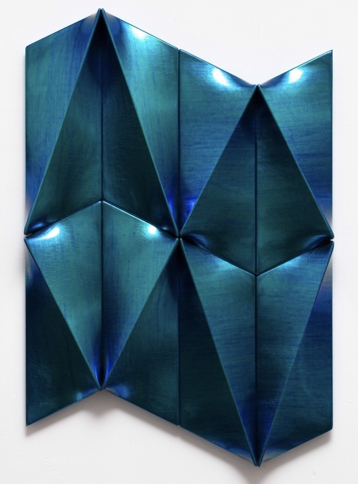 A blue metal sculpture on a white wall. 
