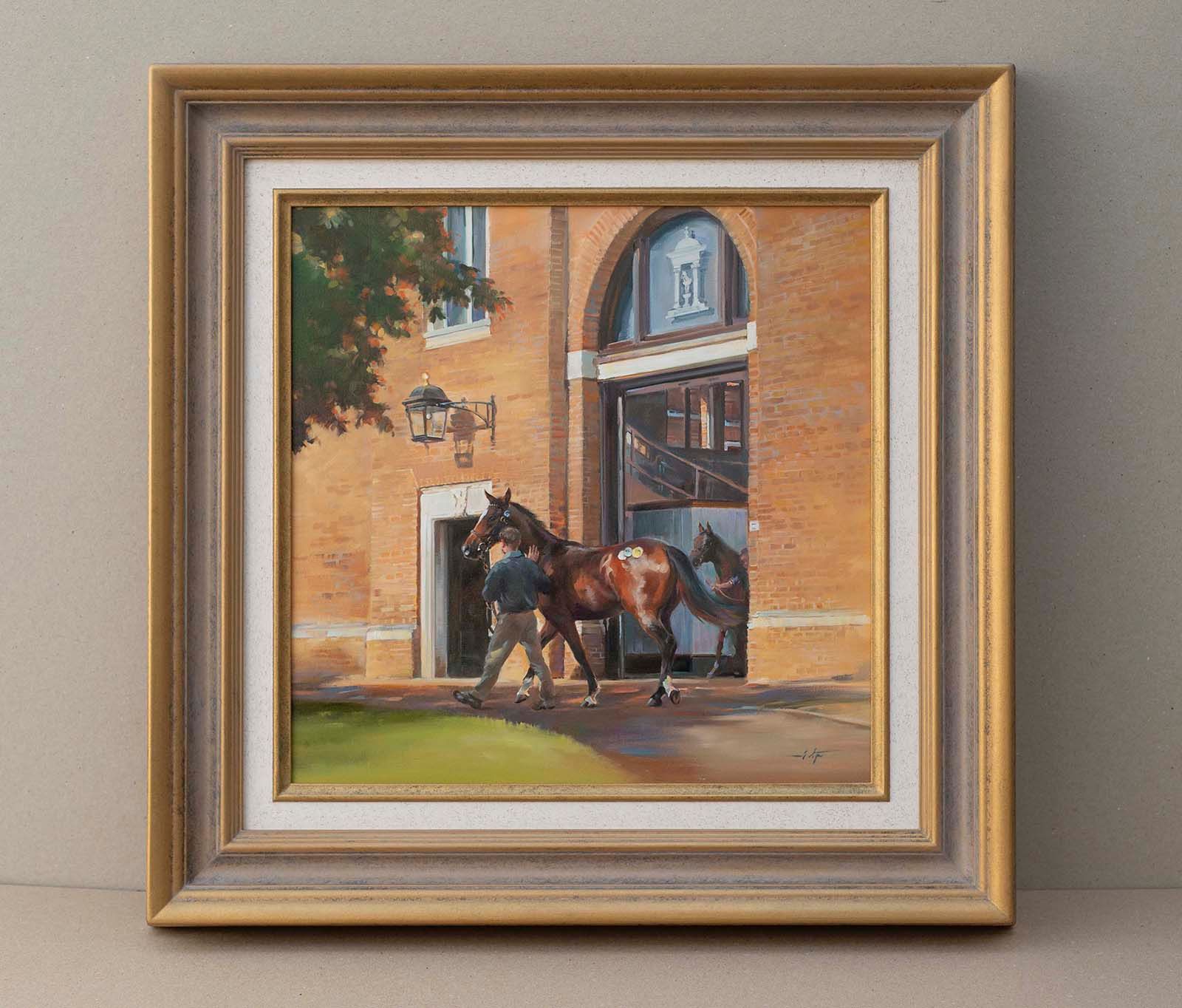 A framed painting of a person leading a horse past a brick building.