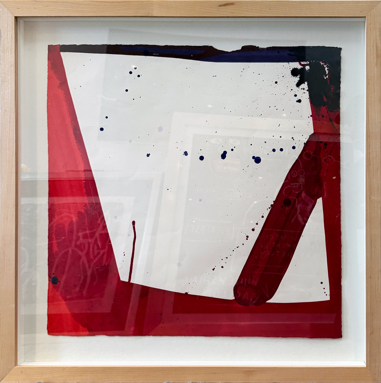 A framed abstract piece featuring bold red and black shapes against a white background with splattered ink.