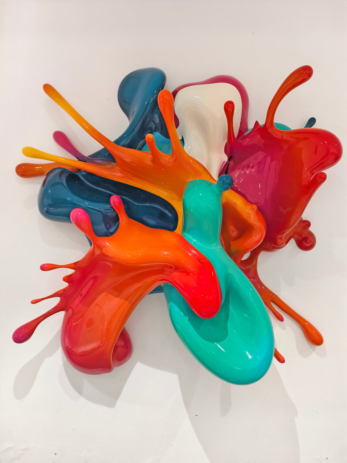 A dynamic sculpture of glossy, multi-colored paint splashes frozen in motion against a plain white background.