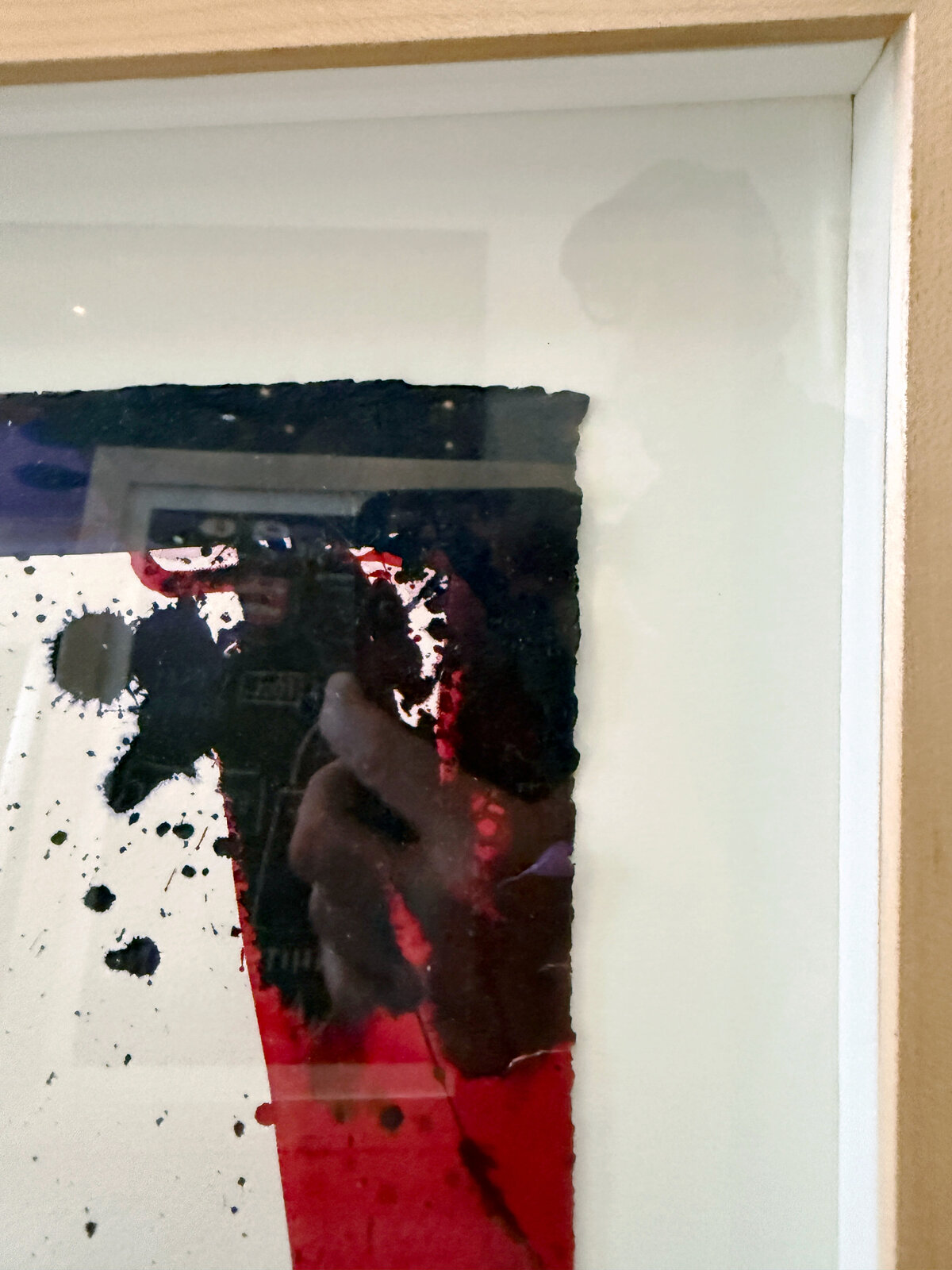 A framed abstract piece featuring bold red and black shapes against a white background with splattered ink.